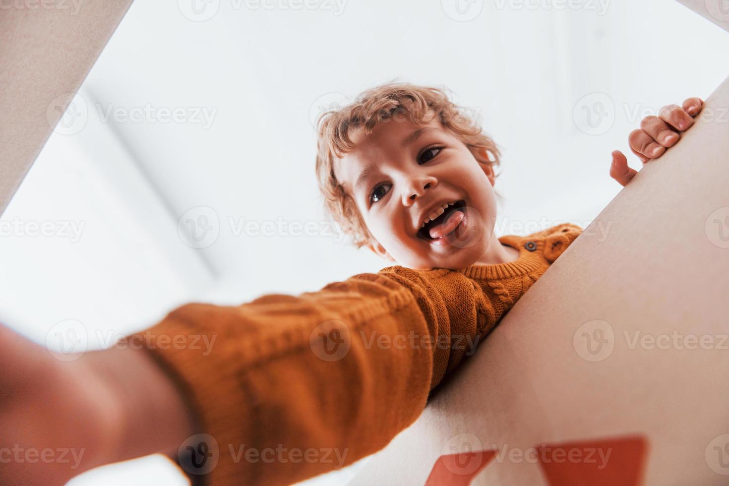 vista desde abajo de un niño con el pelo rizado que se divierte con una caja de papel en el interior foto