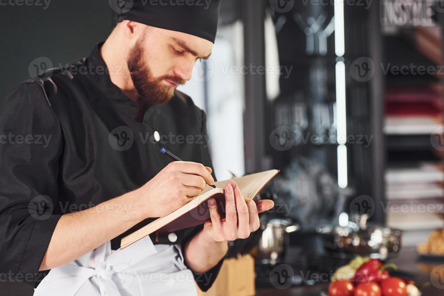 Professional young chef cook in uniform standing with notepad on the kitchen photo