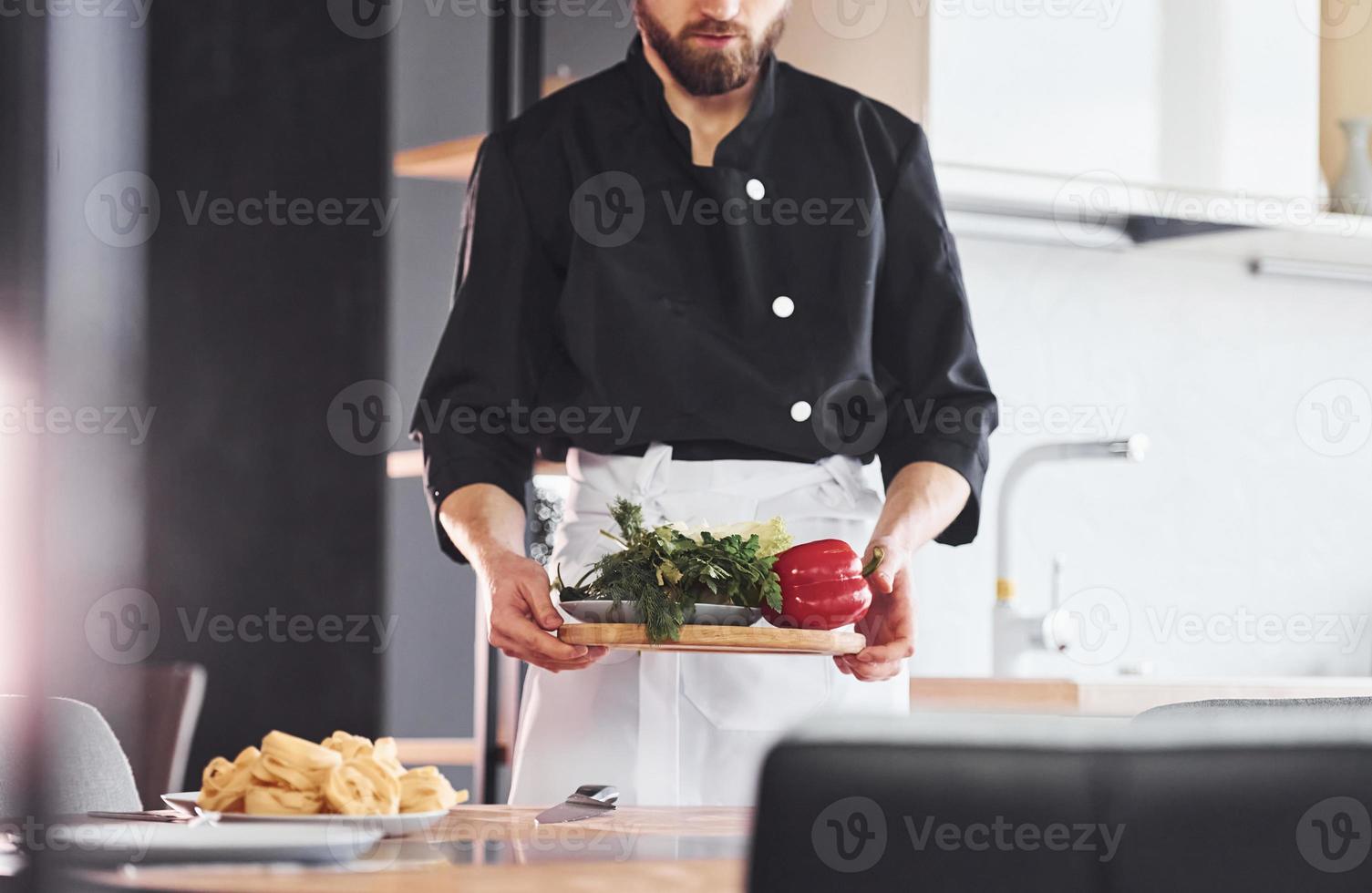 With vegetables. Professional young chef cook in uniform working on the kitchen photo