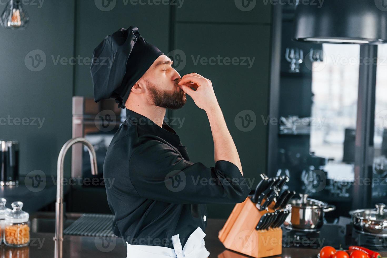 Side view of professional young chef cook in uniform that standing on the kitchen photo