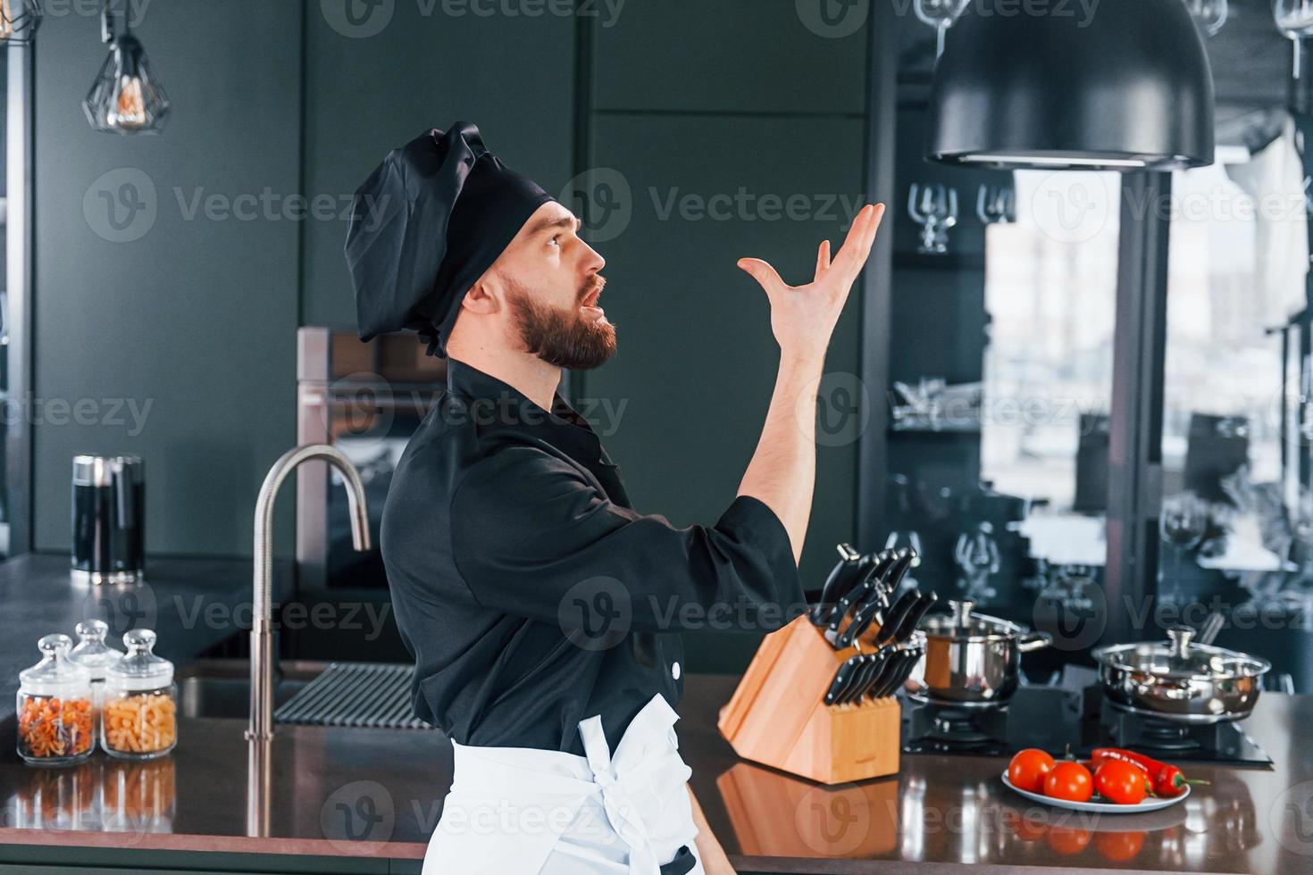 Side view of professional young chef cook in uniform that standing on the kitchen photo