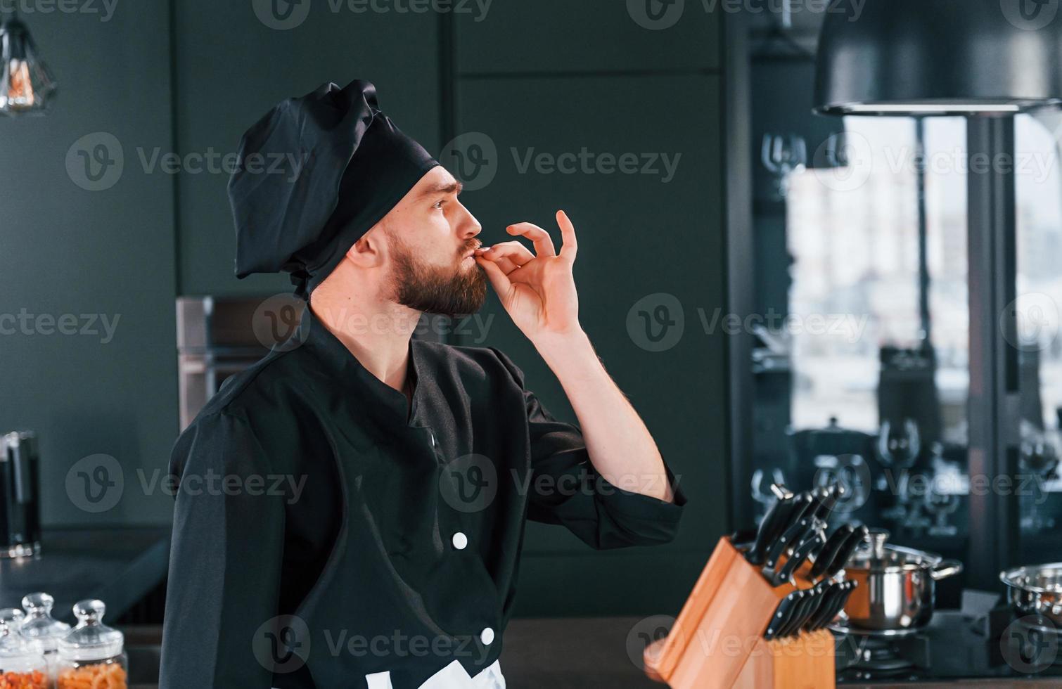 Side view of professional young chef cook in uniform that standing on the kitchen photo