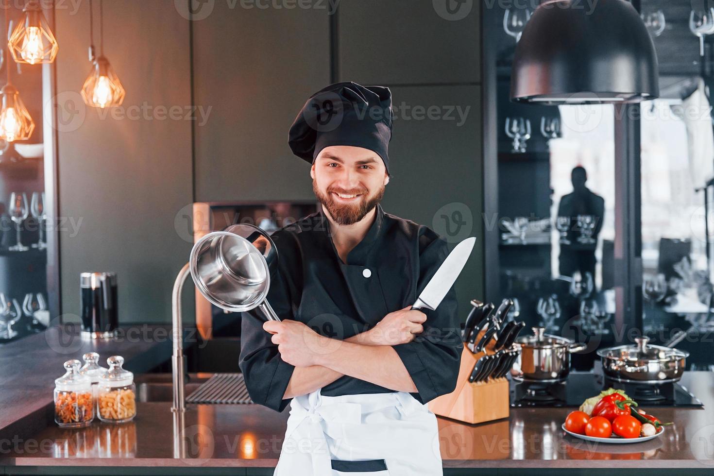 Professional young chef cook in uniform standing near table and posing for a camera on the kitchen photo