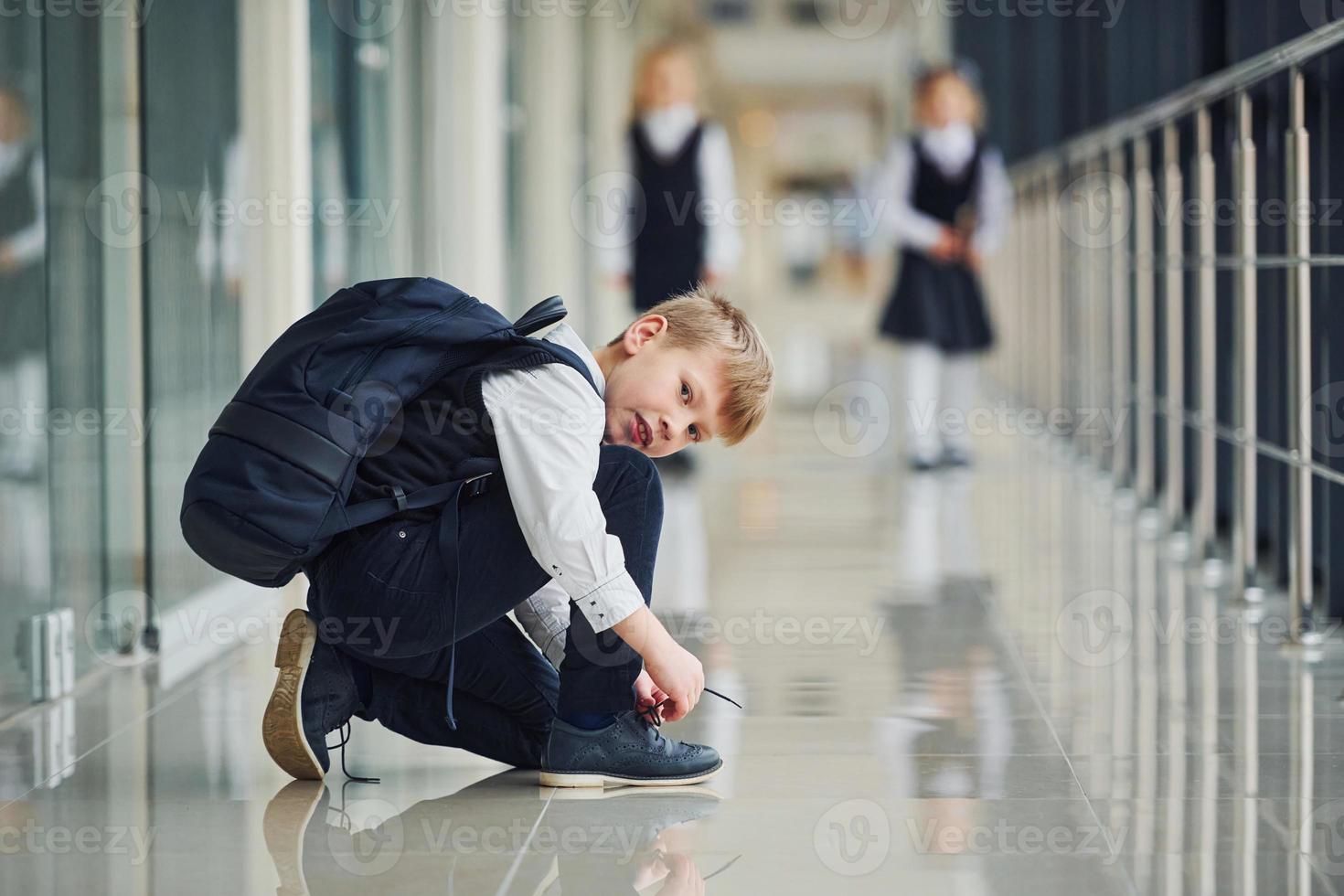 Boy sitting on the floor. School kids in uniform together in corridor photo