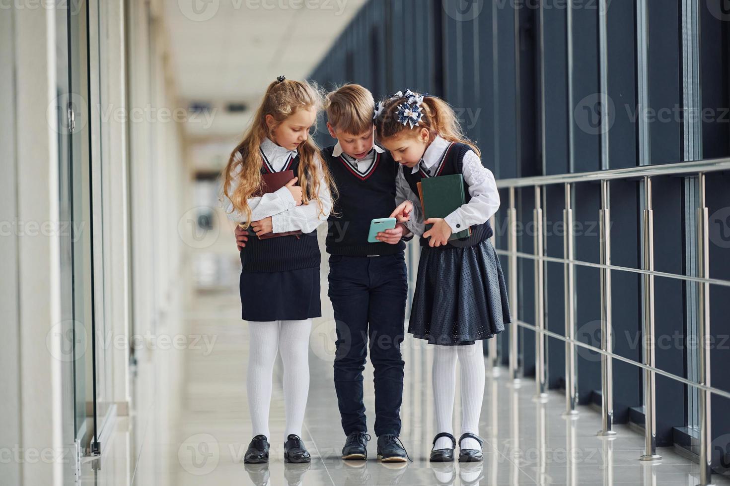 School kids in uniform together with phone in corridor. Conception of education photo
