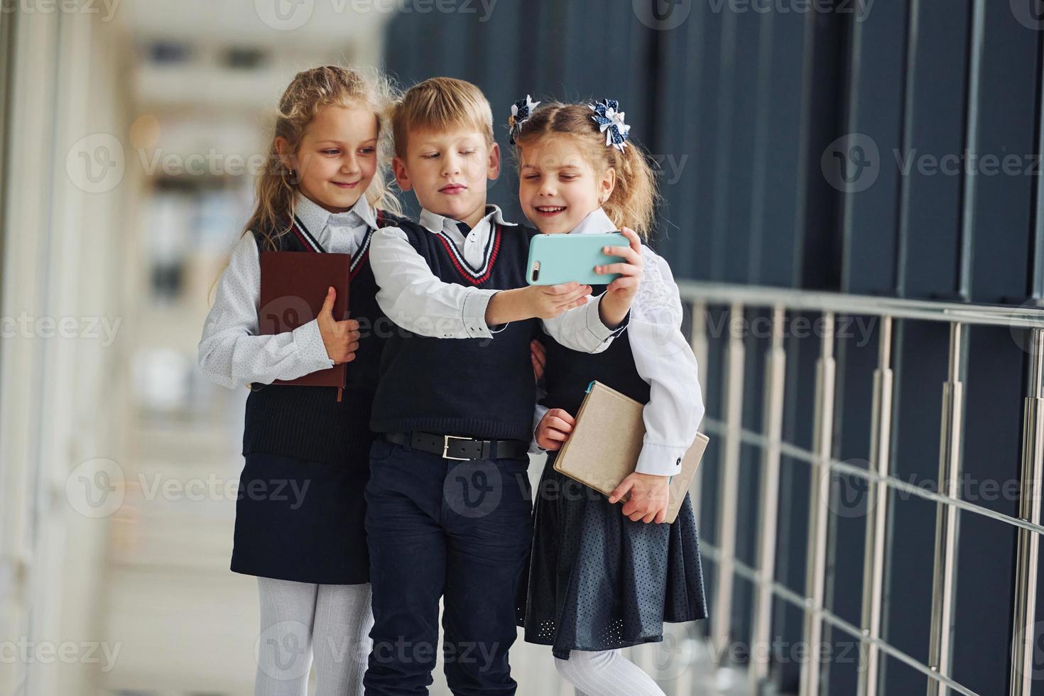 School kids in uniform together with phone and making selfie in corridor. Conception of education photo