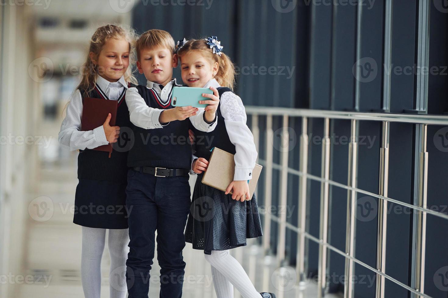 School kids in uniform together with phone and making selfie in corridor. Conception of education photo