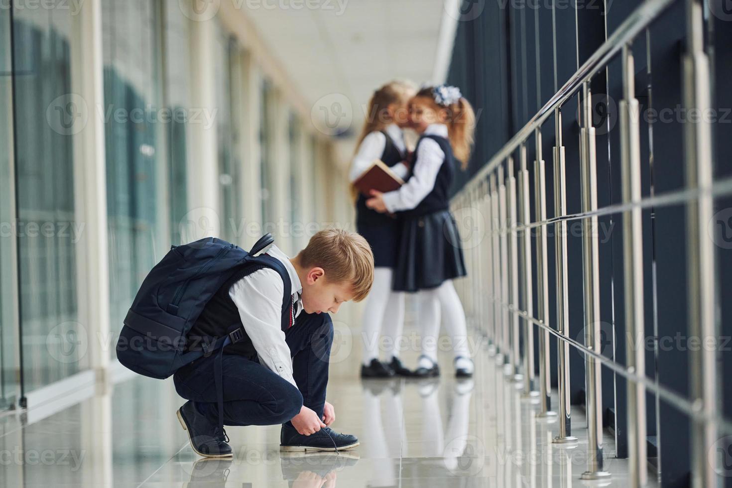 Boy sitting on the floor. School kids in uniform together in corridor photo