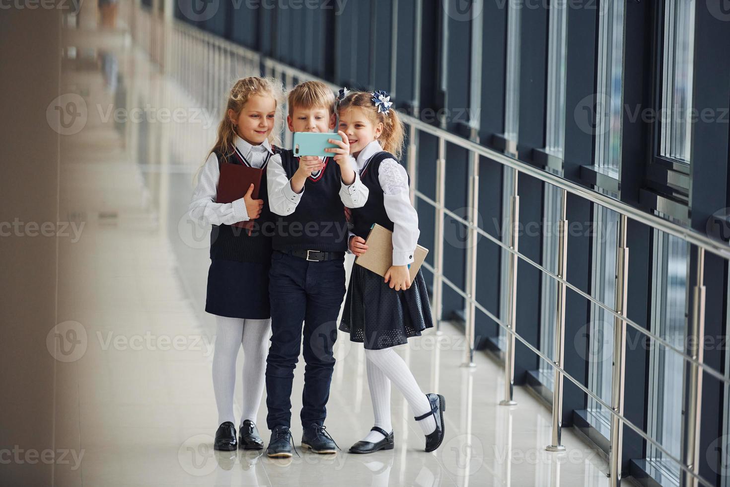 School kids in uniform together with phone and making selfie in corridor. Conception of education photo