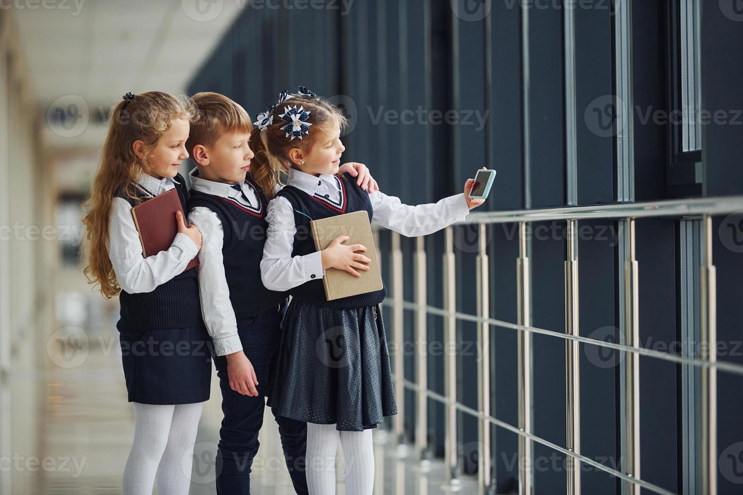 School kids in uniform together with phone and making selfie in corridor. Conception of education photo