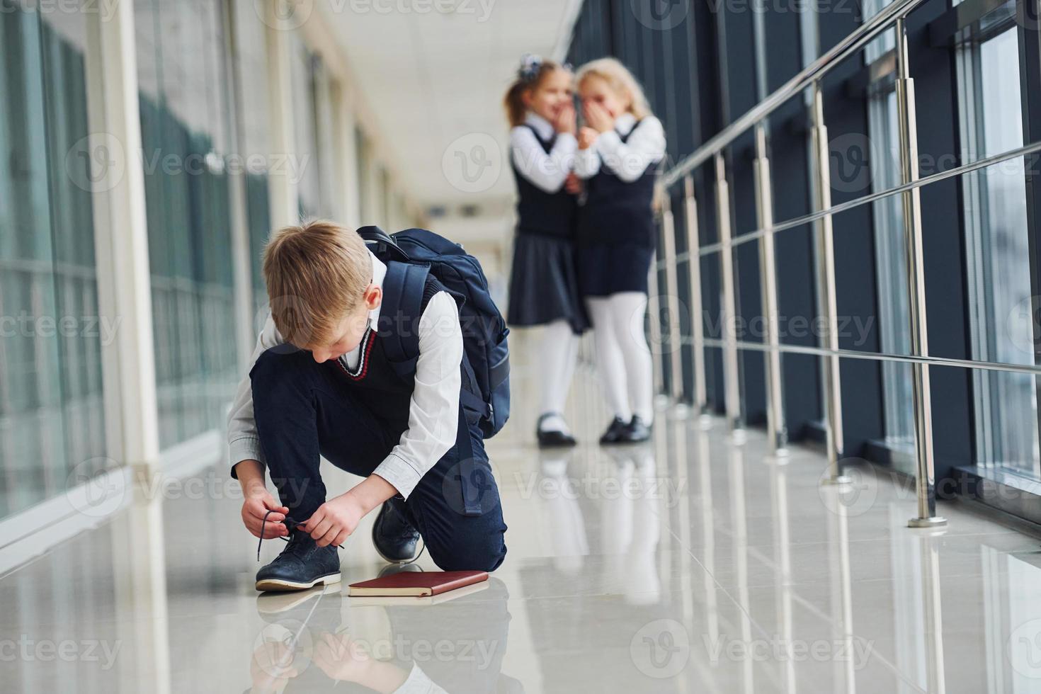 Boy sitting on the floor. School kids in uniform together in corridor photo