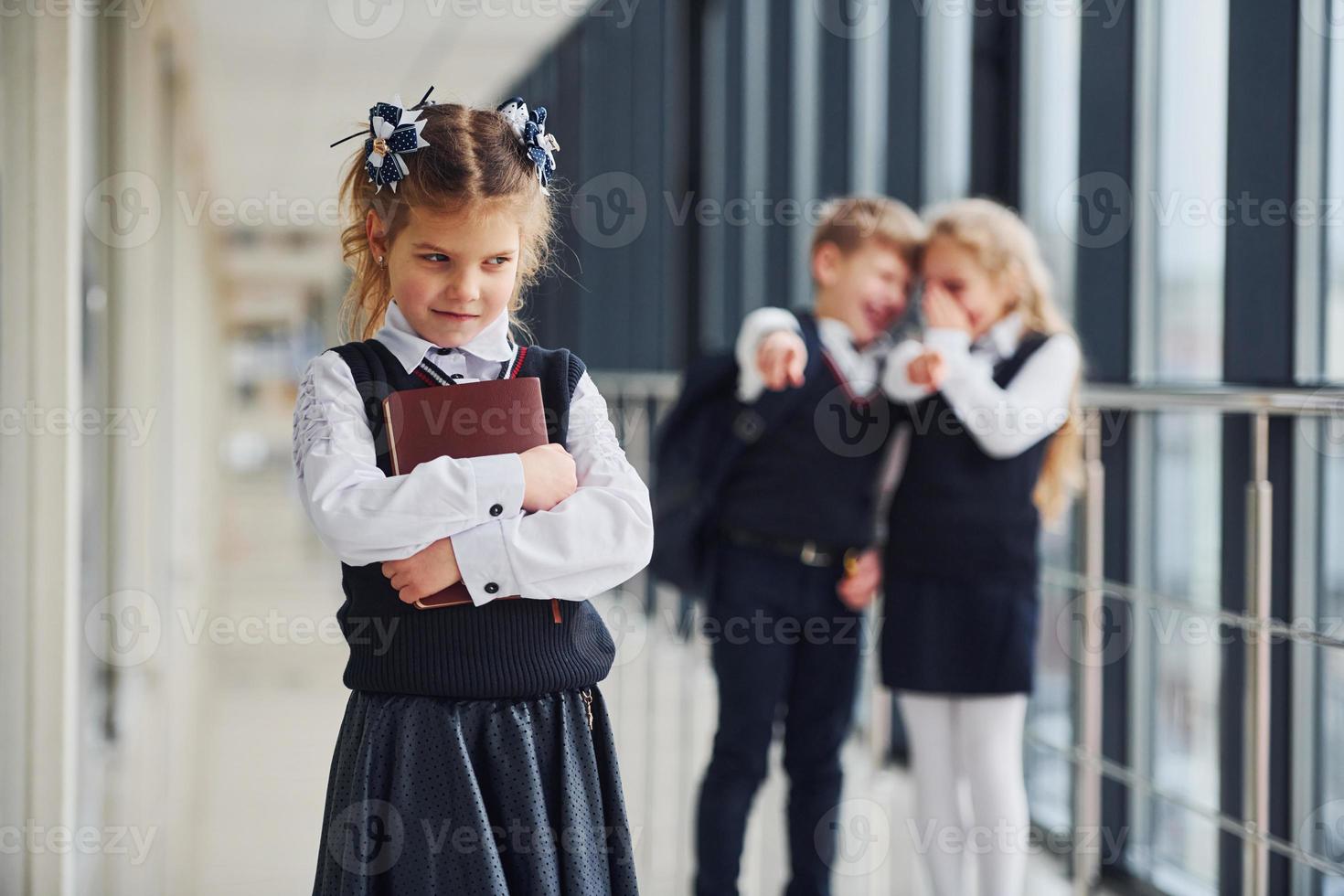 Little girl gets bullied. Conception of harassment. School kids in uniform together in corridor photo