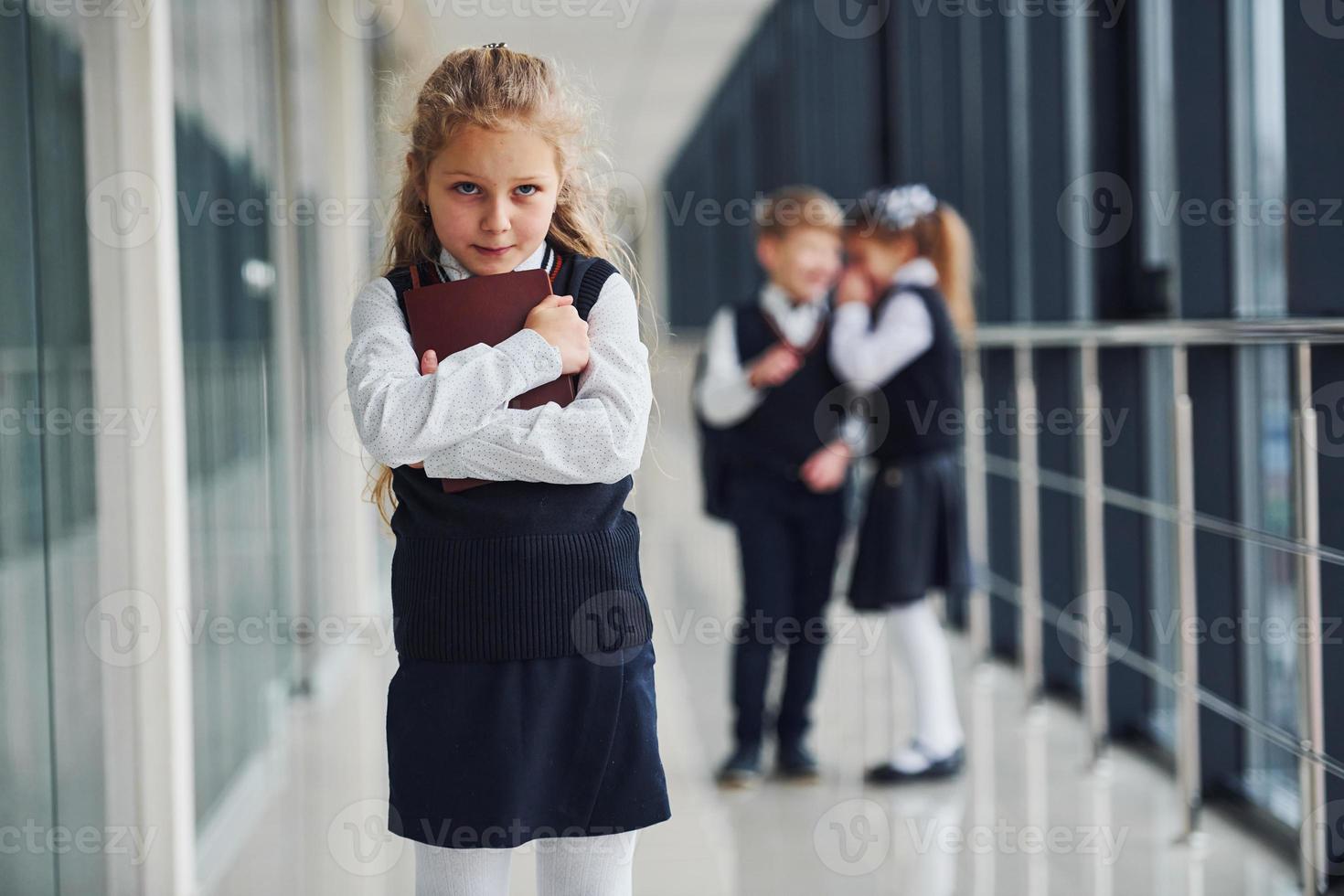 Little girl gets bullied. Conception of harassment. School kids in uniform together in corridor photo