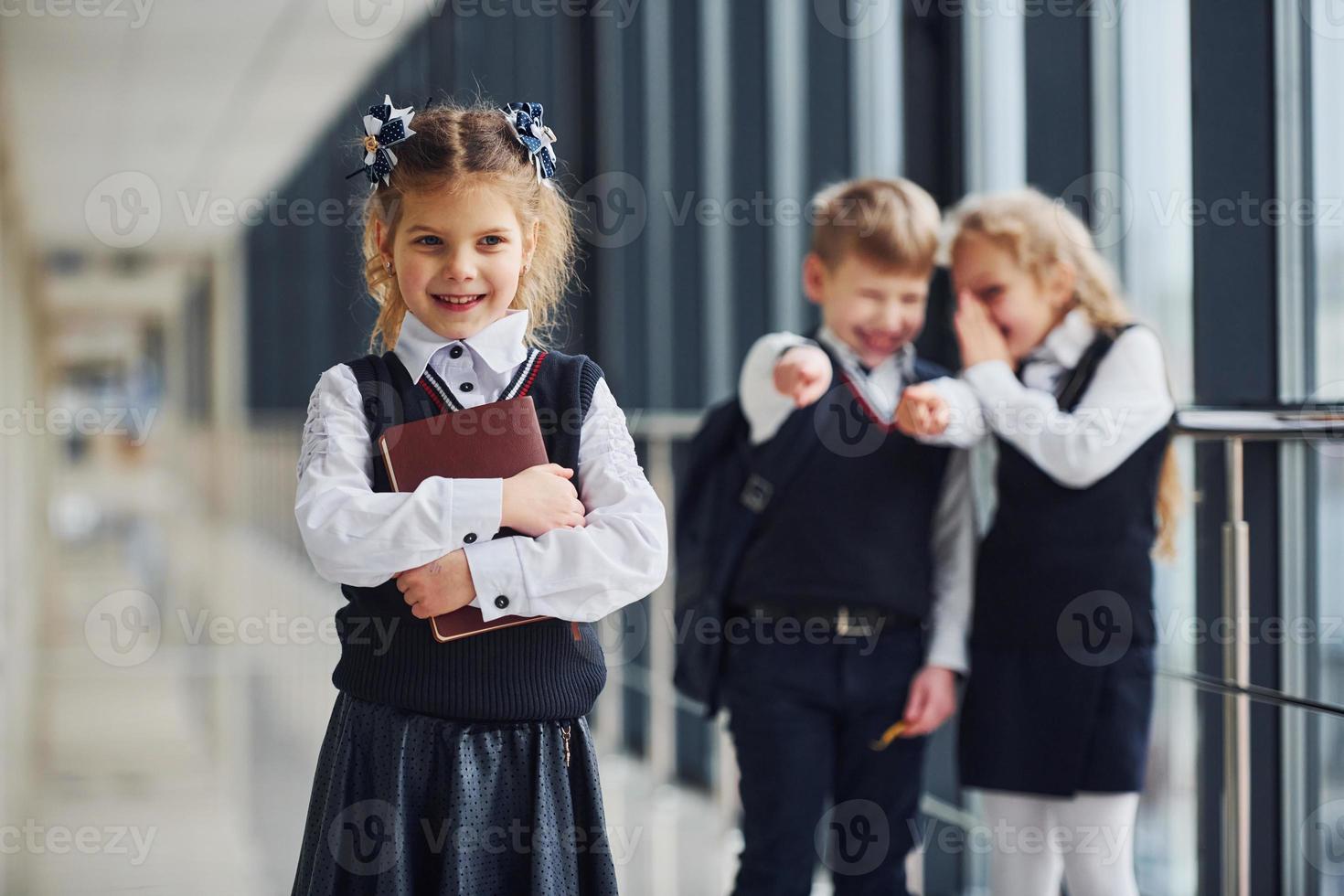 Little girl gets bullied. Conception of harassment. School kids in uniform together in corridor photo