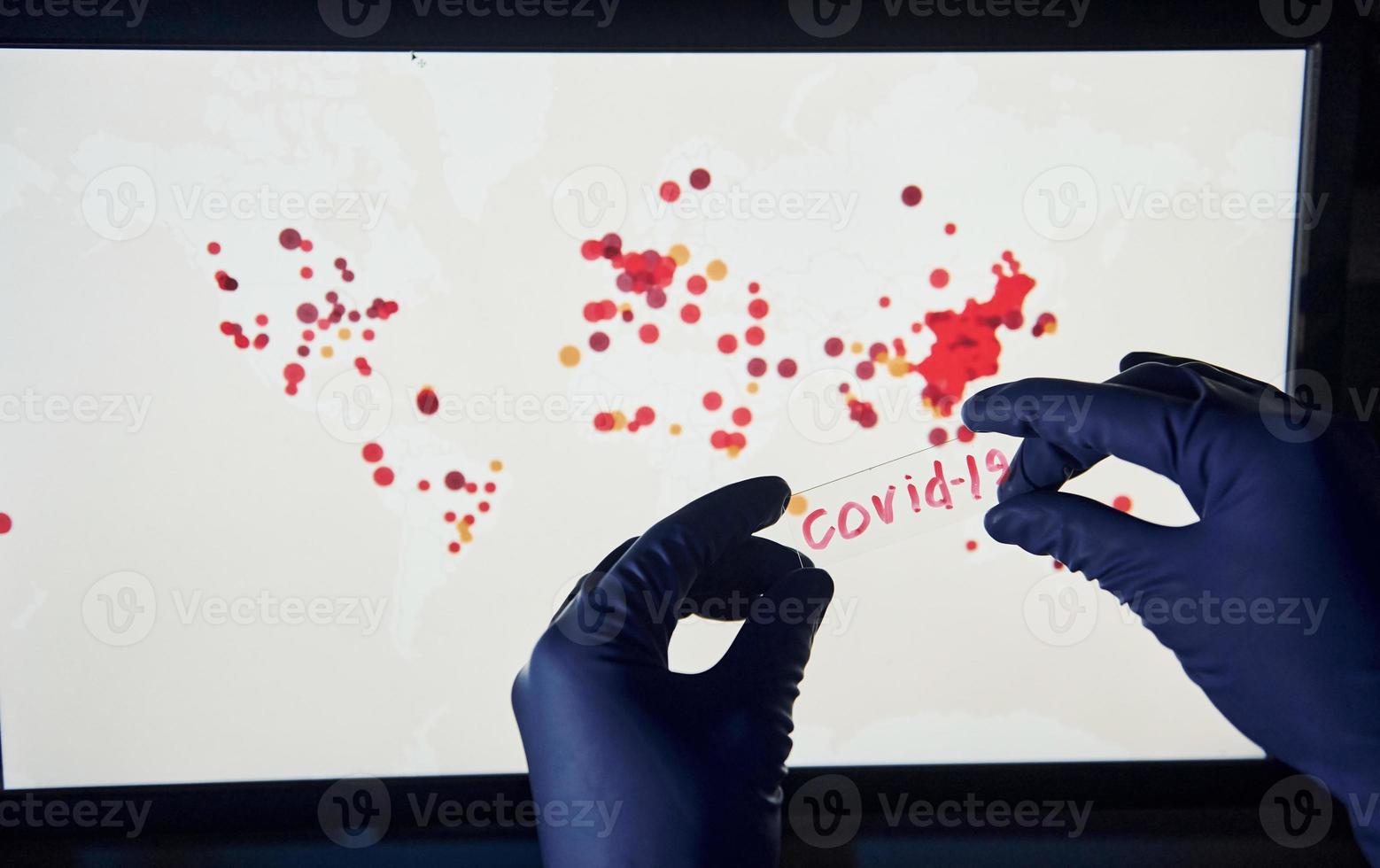 la mano del hombre sostiene una lente con el título covid-19 contra el fondo con un mapa mundial de infección foto