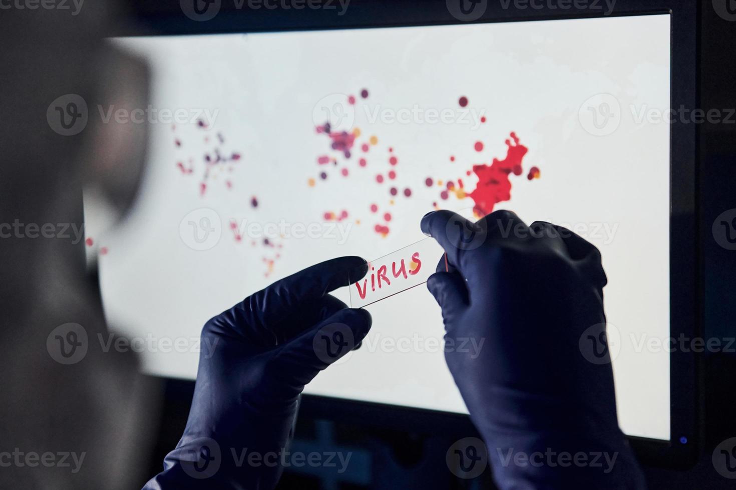 Man's hand holds lens with virus title on it against background with world map of infection photo