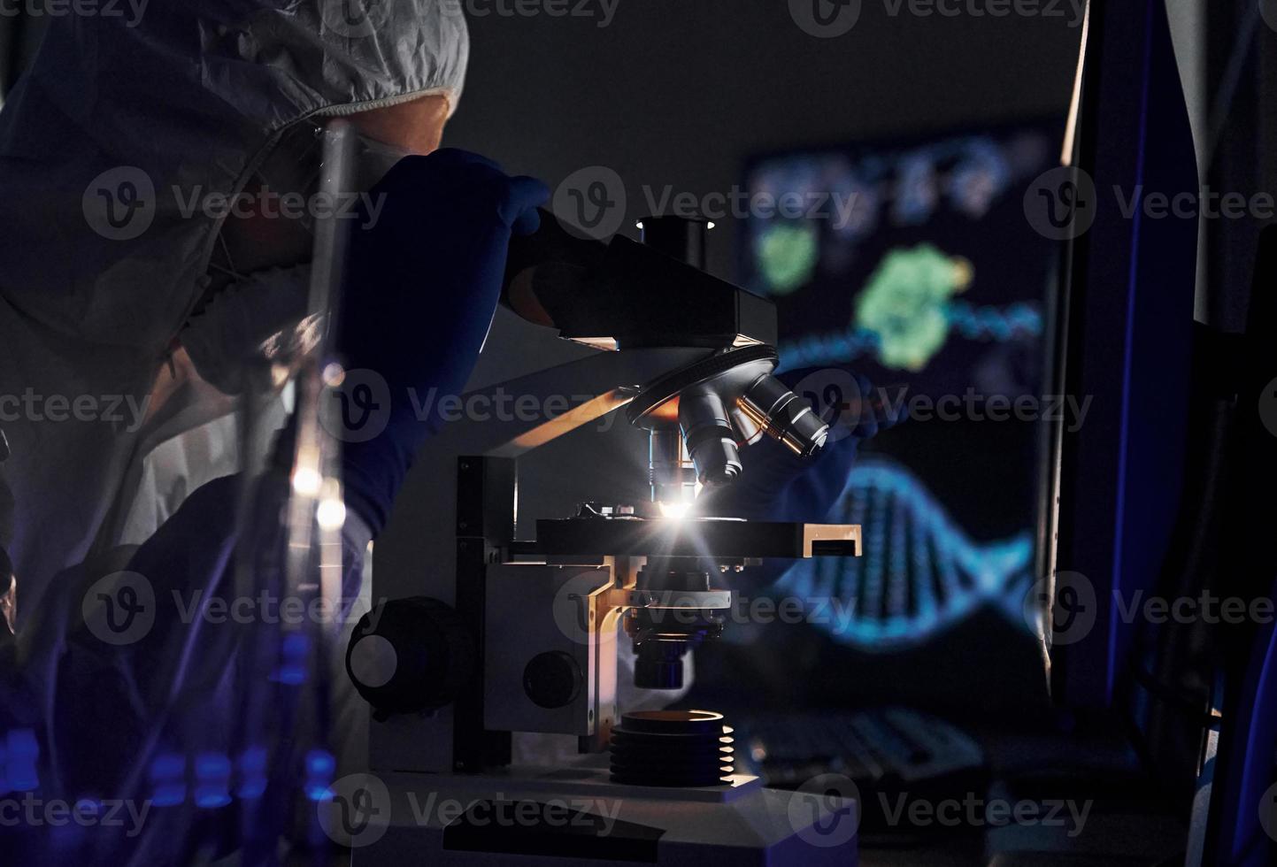 vista lateral del científico con uniforme protector blanco que trabaja con coronavirus en laboratorio foto