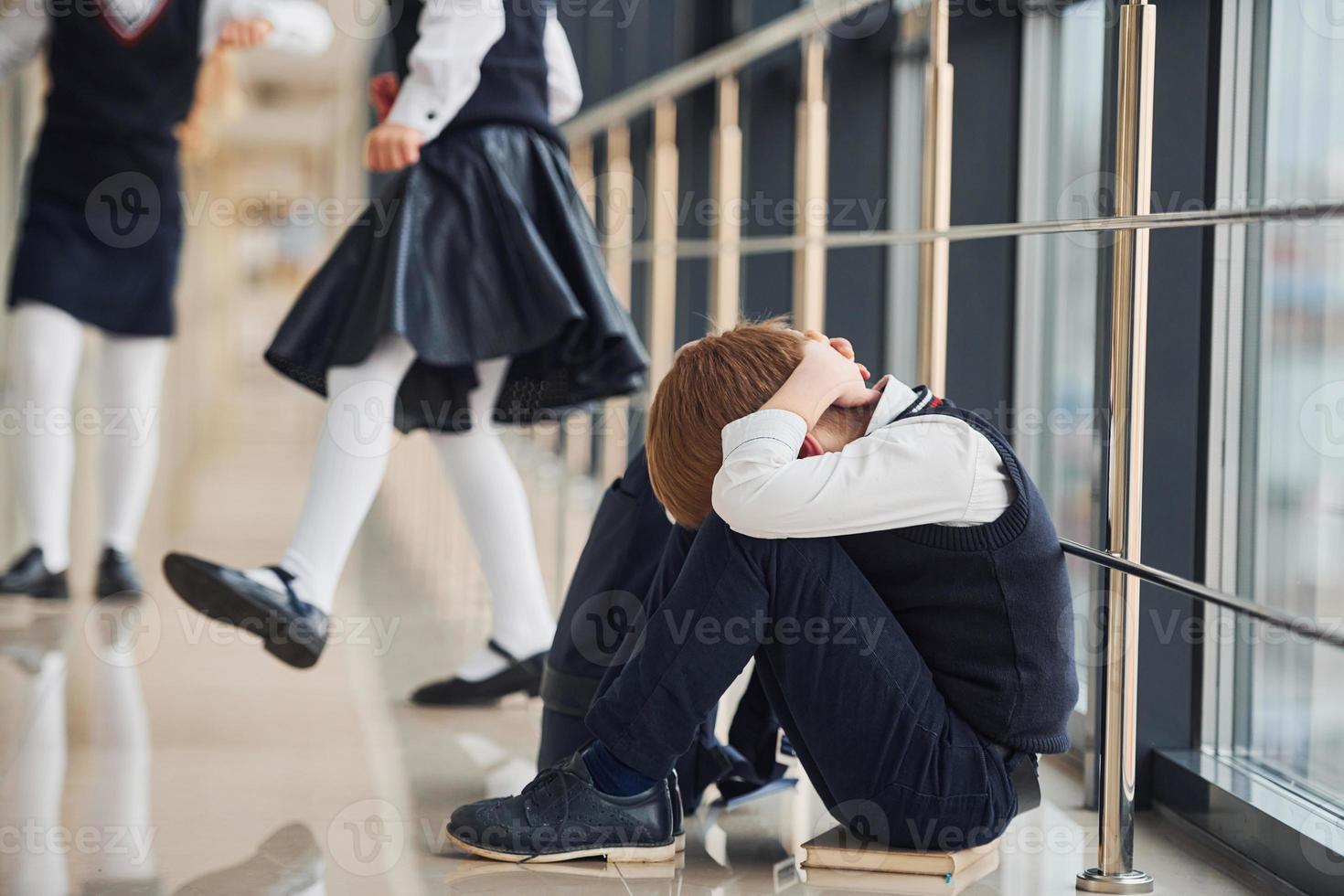 niño en uniforme sentado solo sintiéndose triste en la escuela. concepto de acoso foto