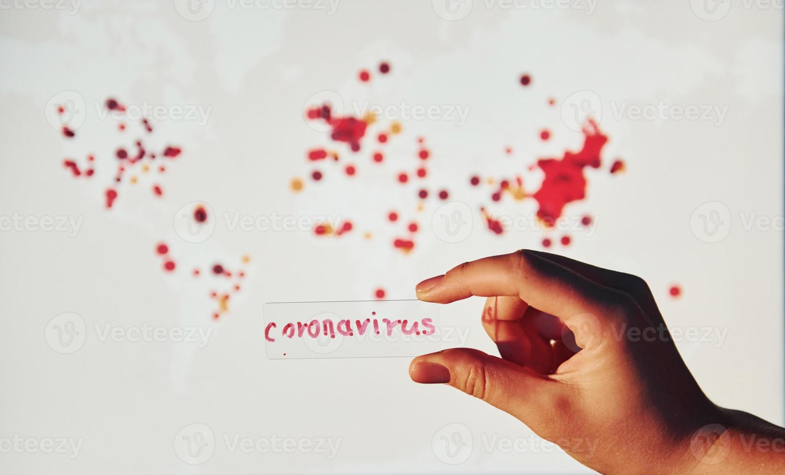 Man's hand holds lens with coronavirus title on it against background with world map of infection photo