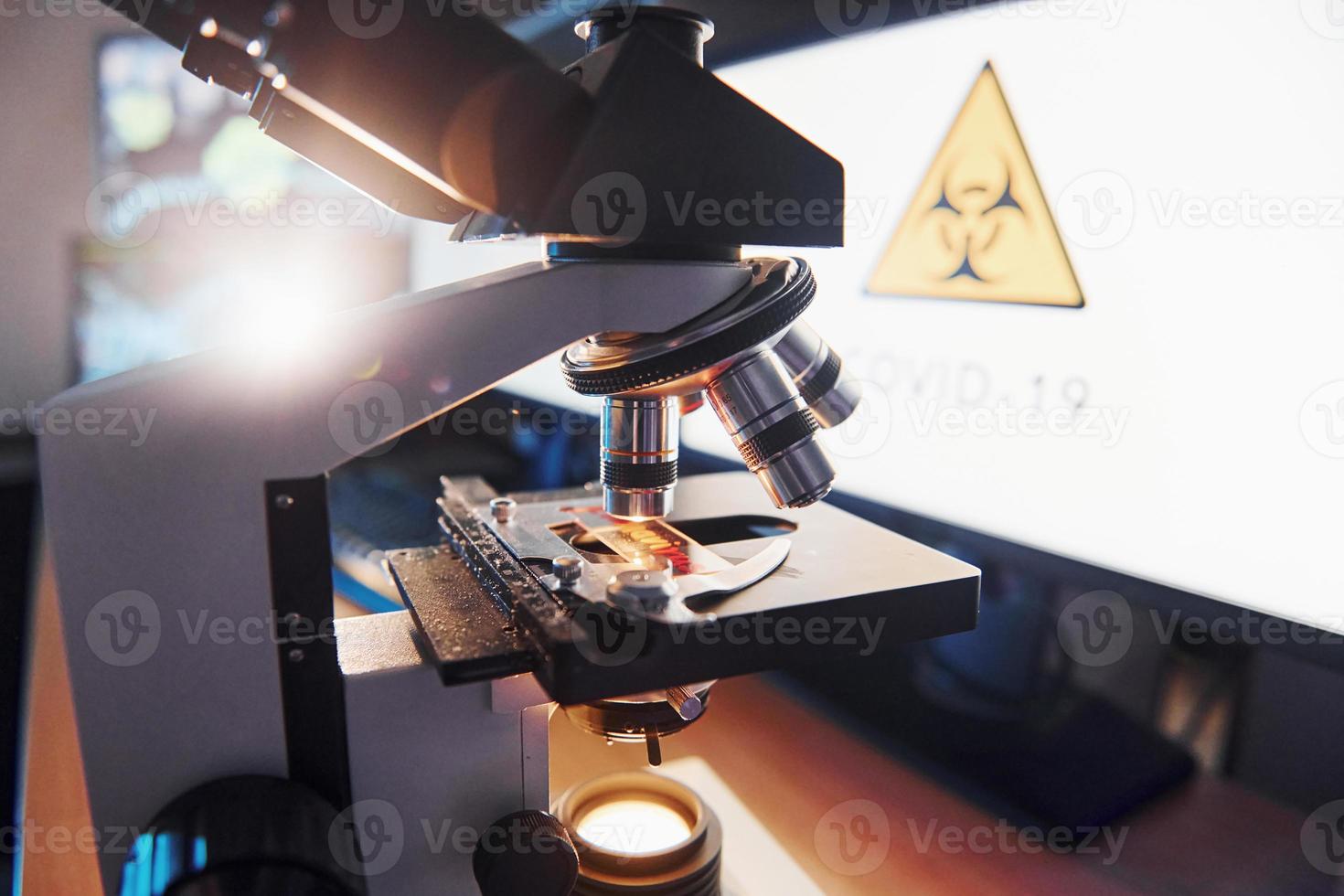 vista de cerca del microscopio moderno en el interior del laboratorio con monitores. concepción del coronavirus foto