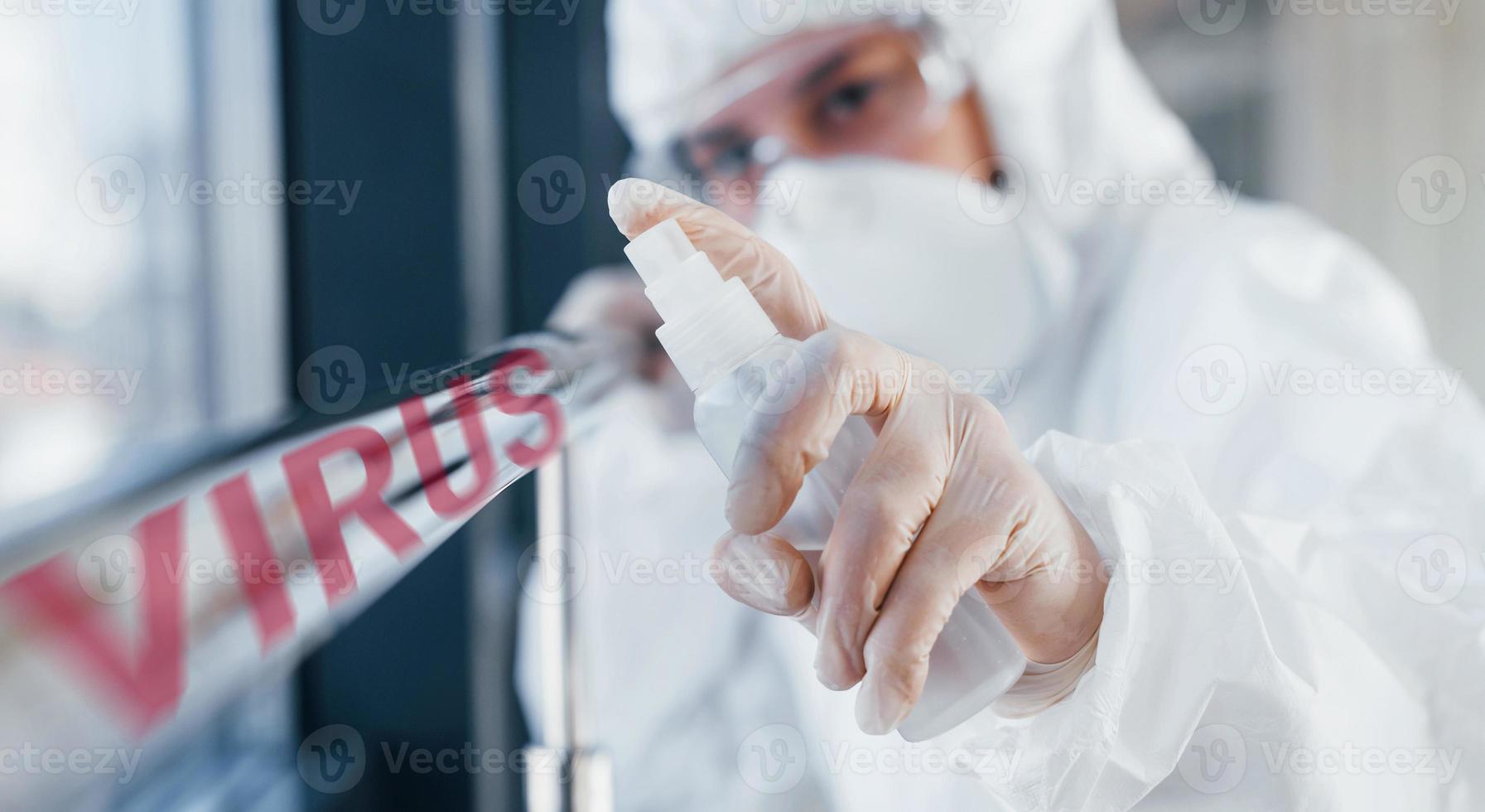 Red virus word. Nurse in protective uniform, mask and glasses standing indoors photo