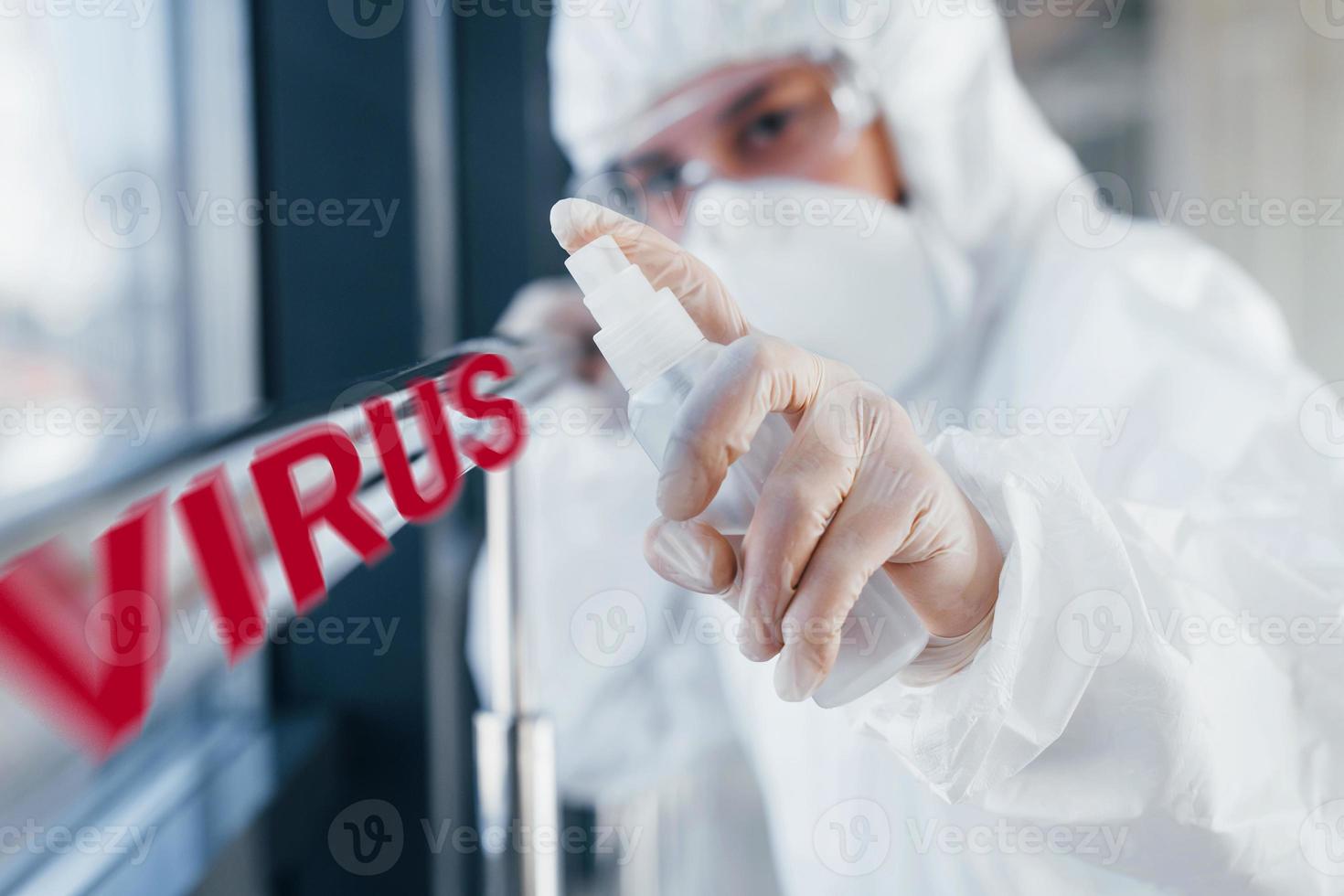 Red virus word. Nurse in protective uniform, mask and glasses standing indoors photo