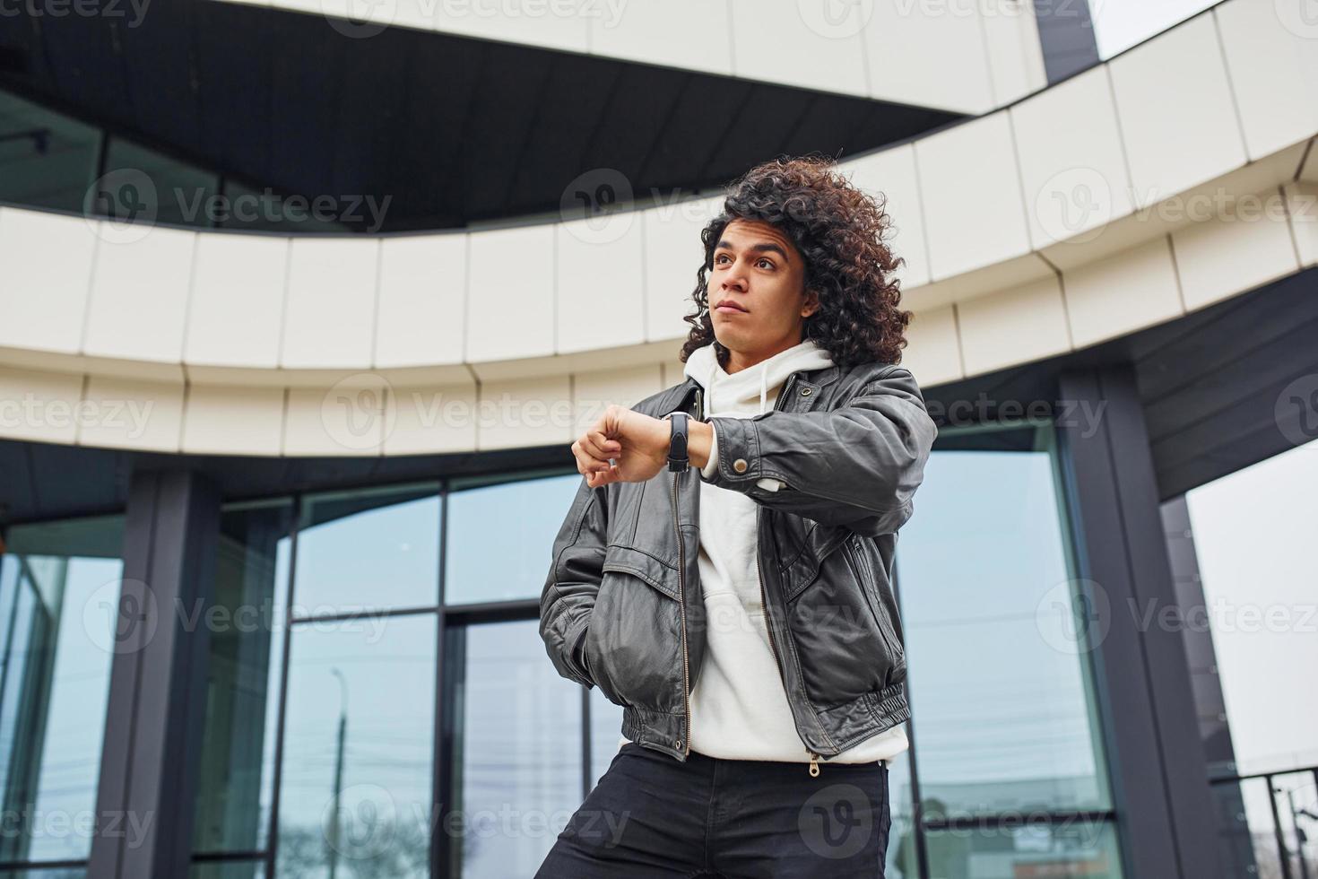 Handsome young man with curly black hair posing for the camera on the street against building photo