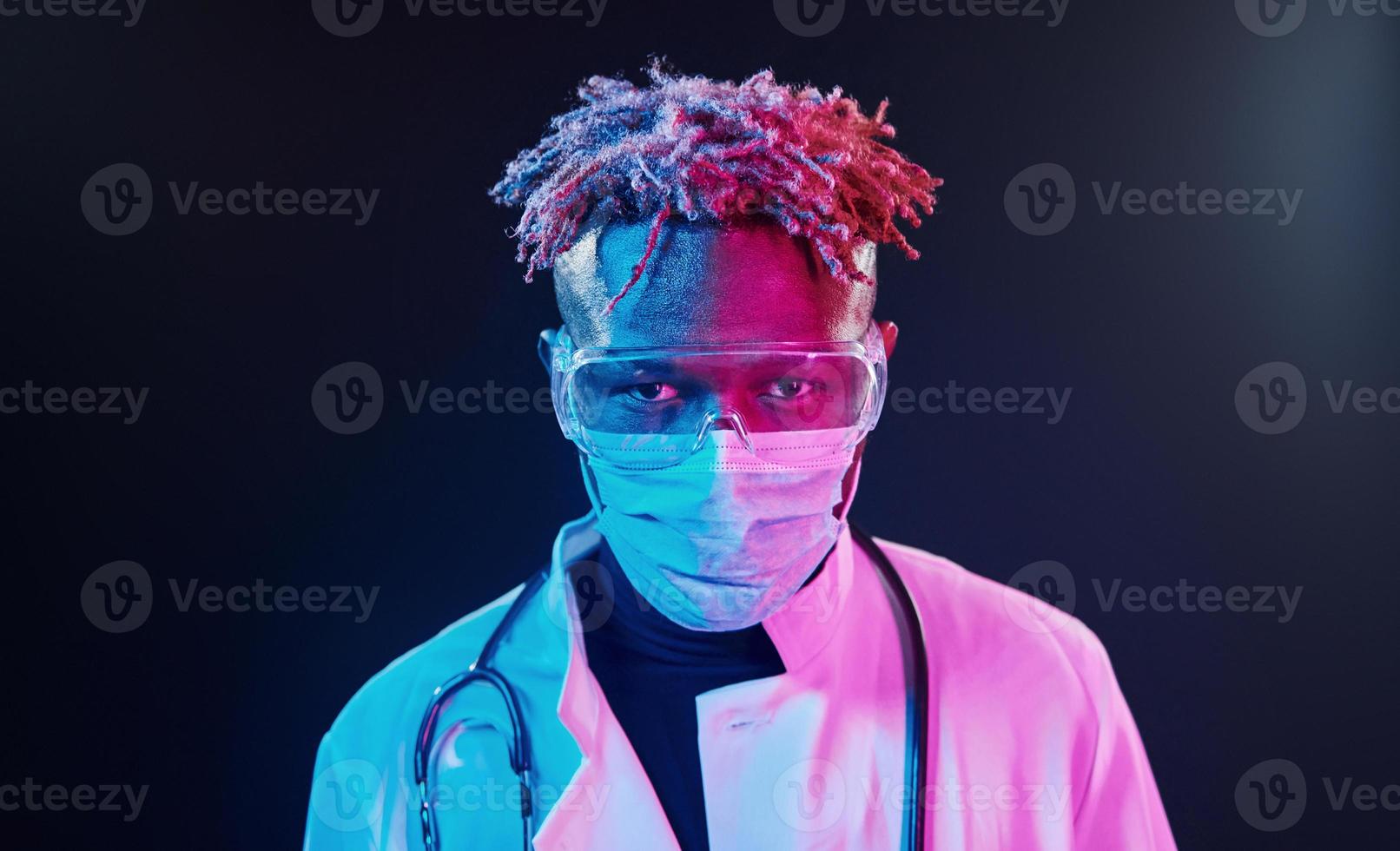 Portrait of doctor in protective uniform. Futuristic neon lighting. Young african american man in the studio photo