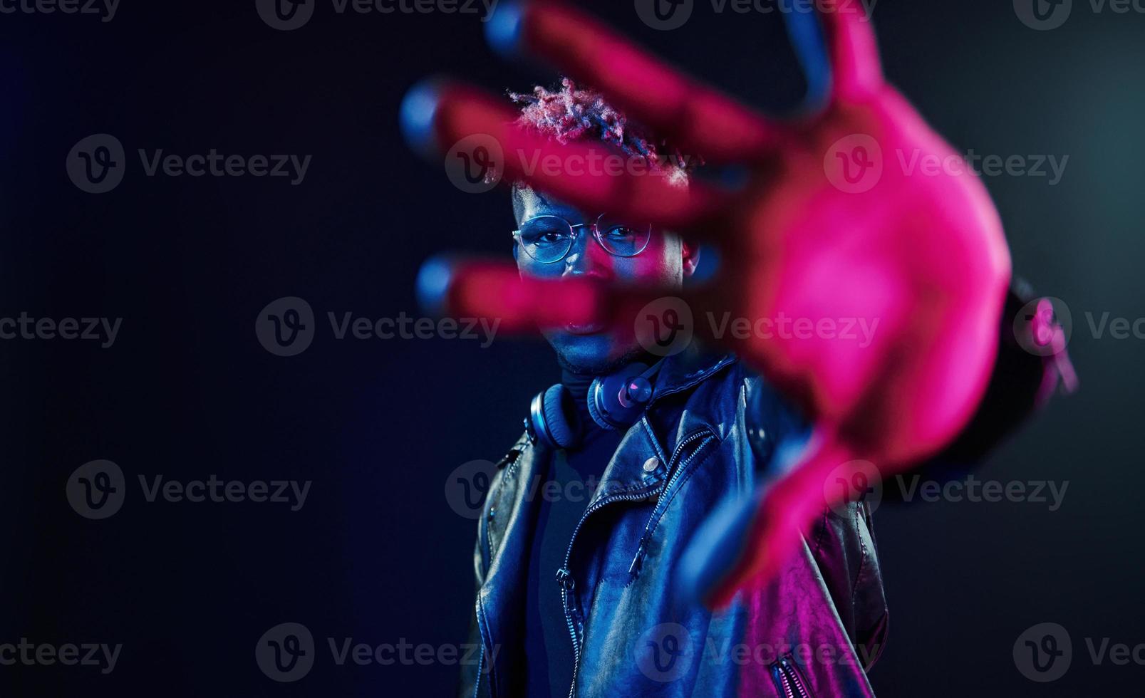 Stylish glasses and wireless headphones. Futuristic neon lighting. Young african american man in the studio photo