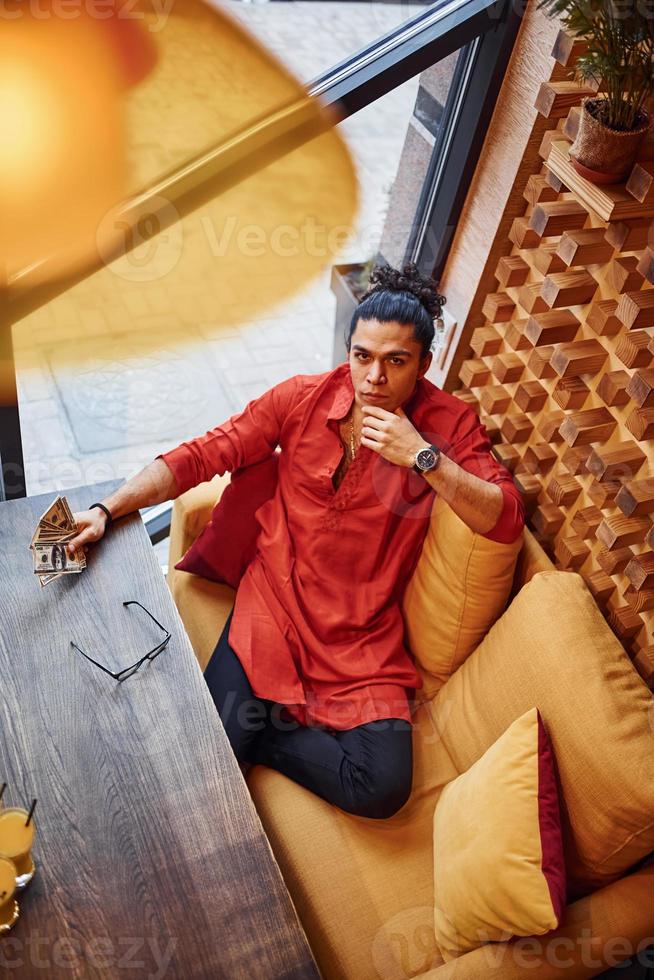 Top view of rich man in red and black clothes that sitting indoors in cafe with lot of money in hand photo