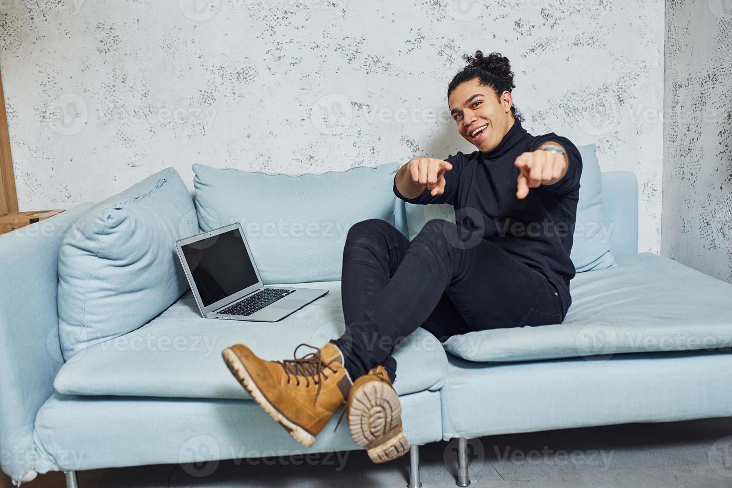 Handsome young man with curly black hair indoors with laptop have fun photo