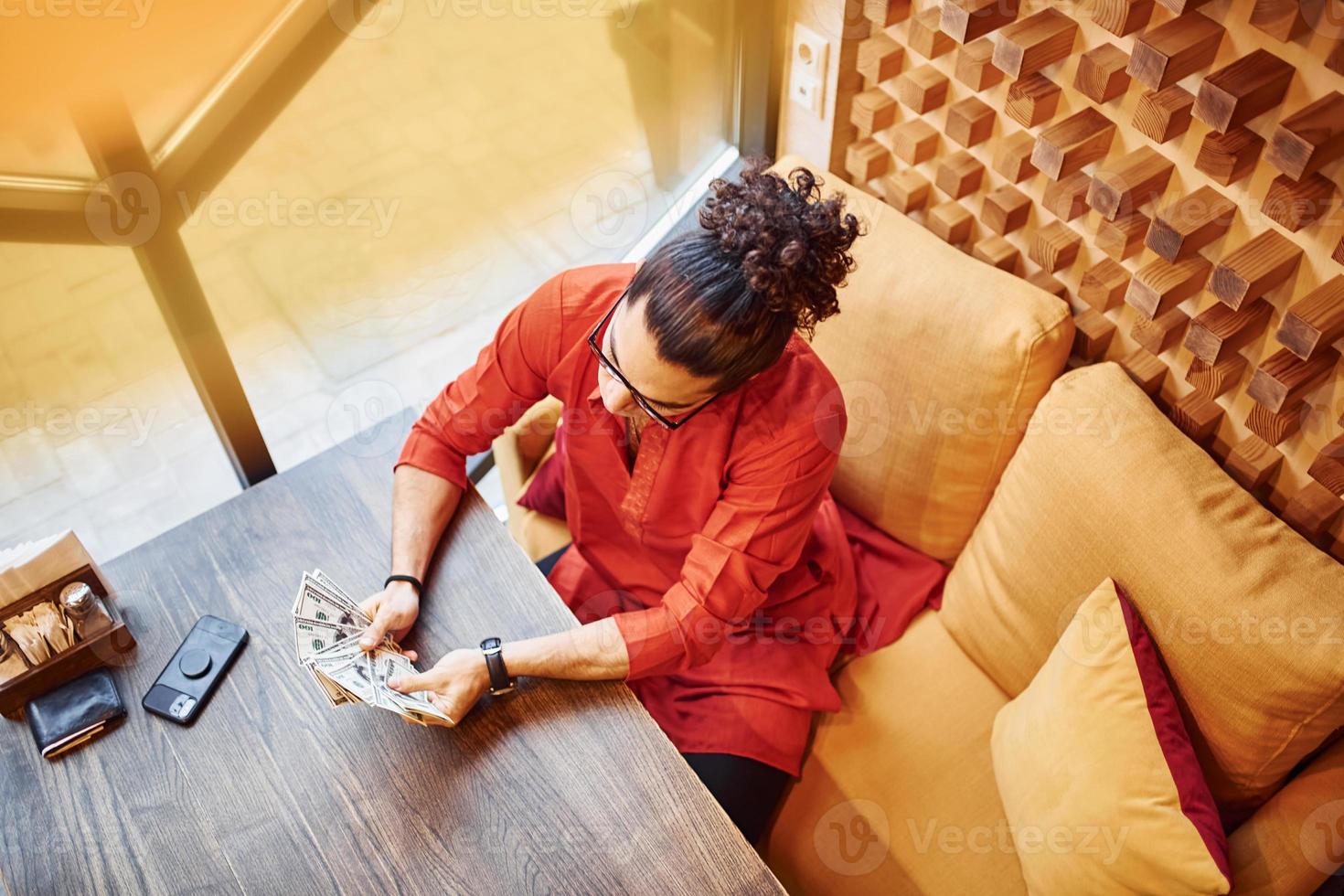 vista superior de un hombre rico vestido de rojo y negro que se sienta en el interior de un café con mucho dinero en las manos foto