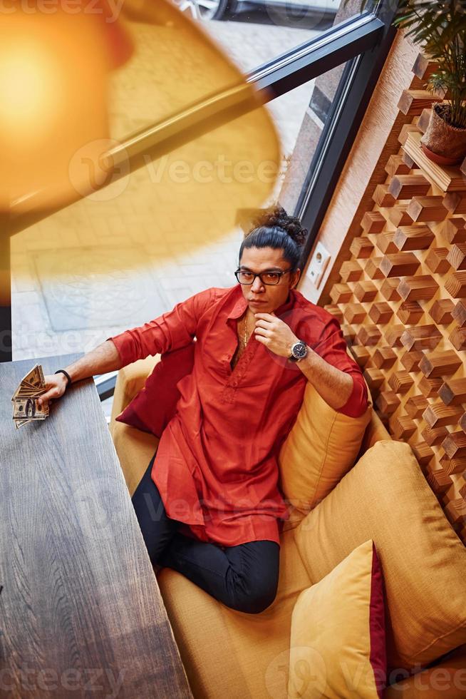 Top view of rich man in red and black clothes that sitting indoors in cafe with lot of money in hand photo