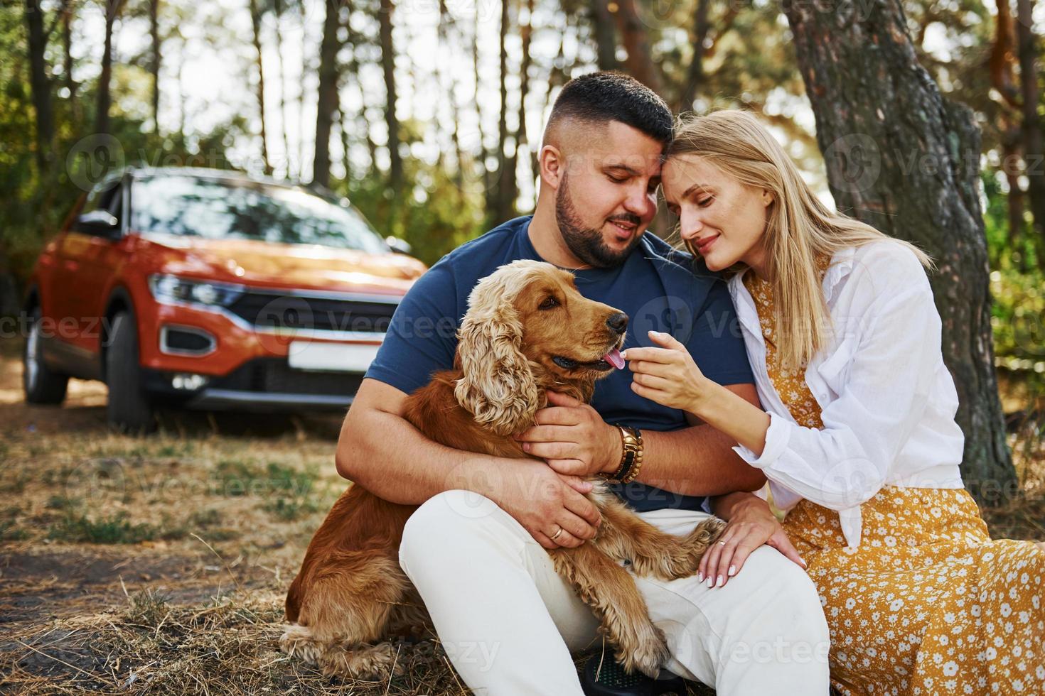 Couple with dog have weekend outdoors in the forest with car behind them photo