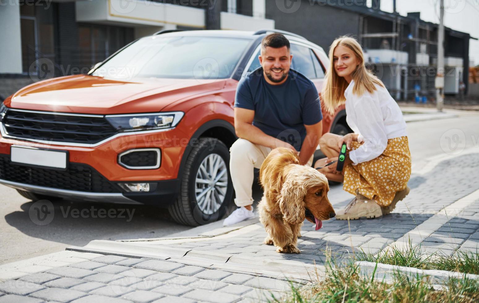 Sits down with pet. Lovely couple have a walk together with dog outdoors near the car photo