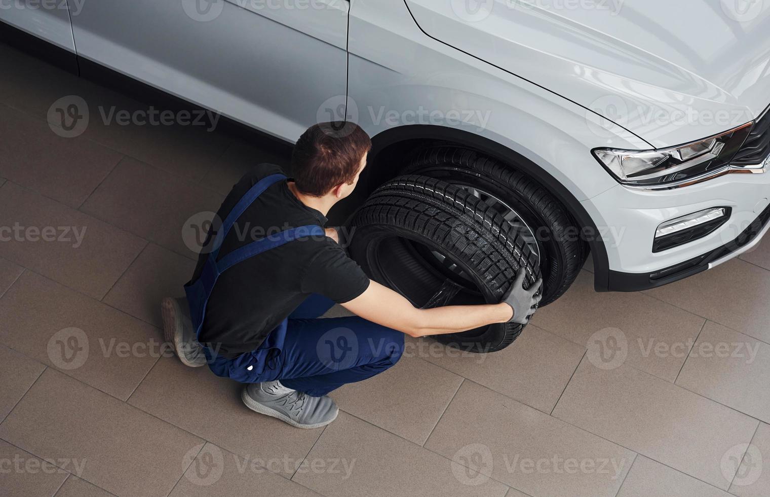 Top view of worker in black and blue uniform that is with car wheel working indoors photo