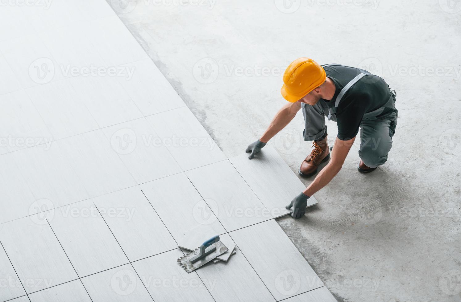 Installation of plates. Man in grey uniform and orange hard hat works indoors in modern big office at daytime photo