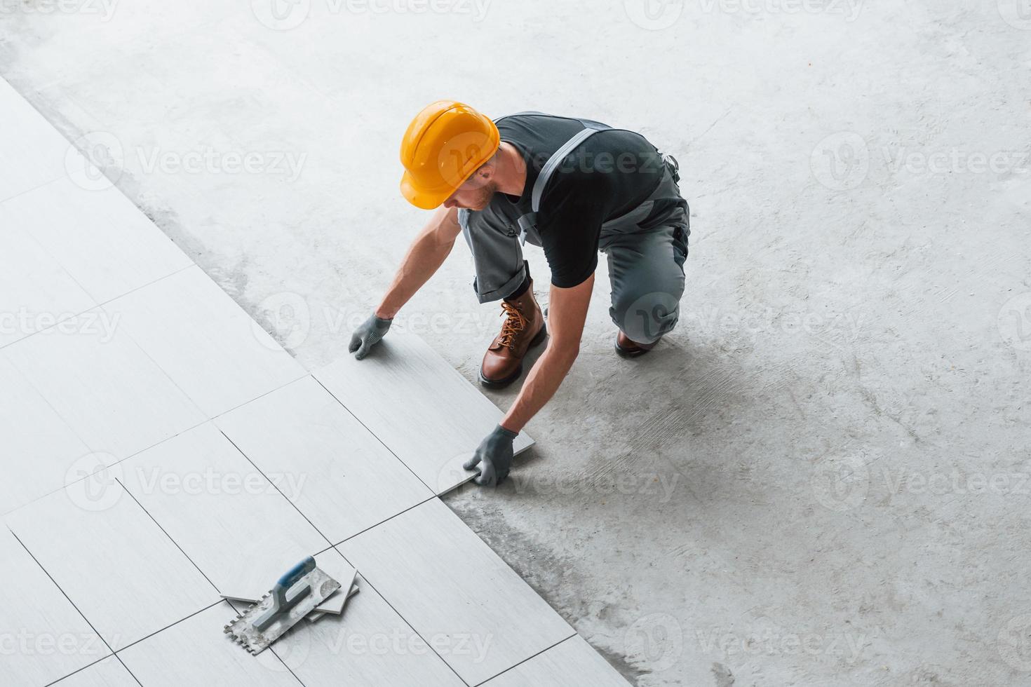 Installation of plates. Man in grey uniform and orange hard hat works indoors in modern big office at daytime photo