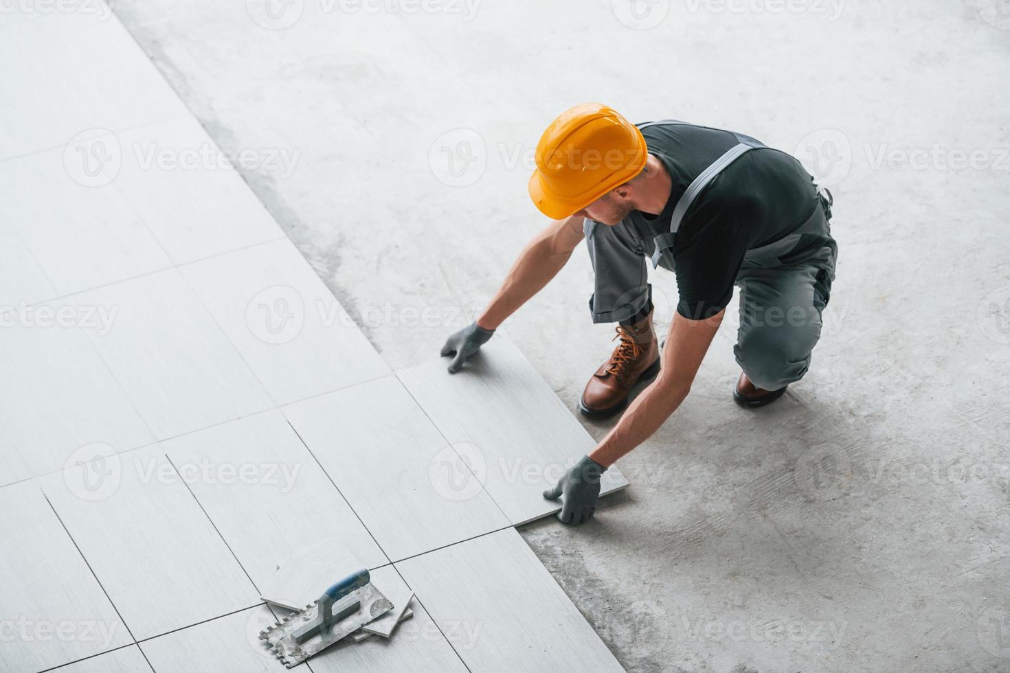Installation of plates. Man in grey uniform and orange hard hat works indoors in modern big office at daytime photo