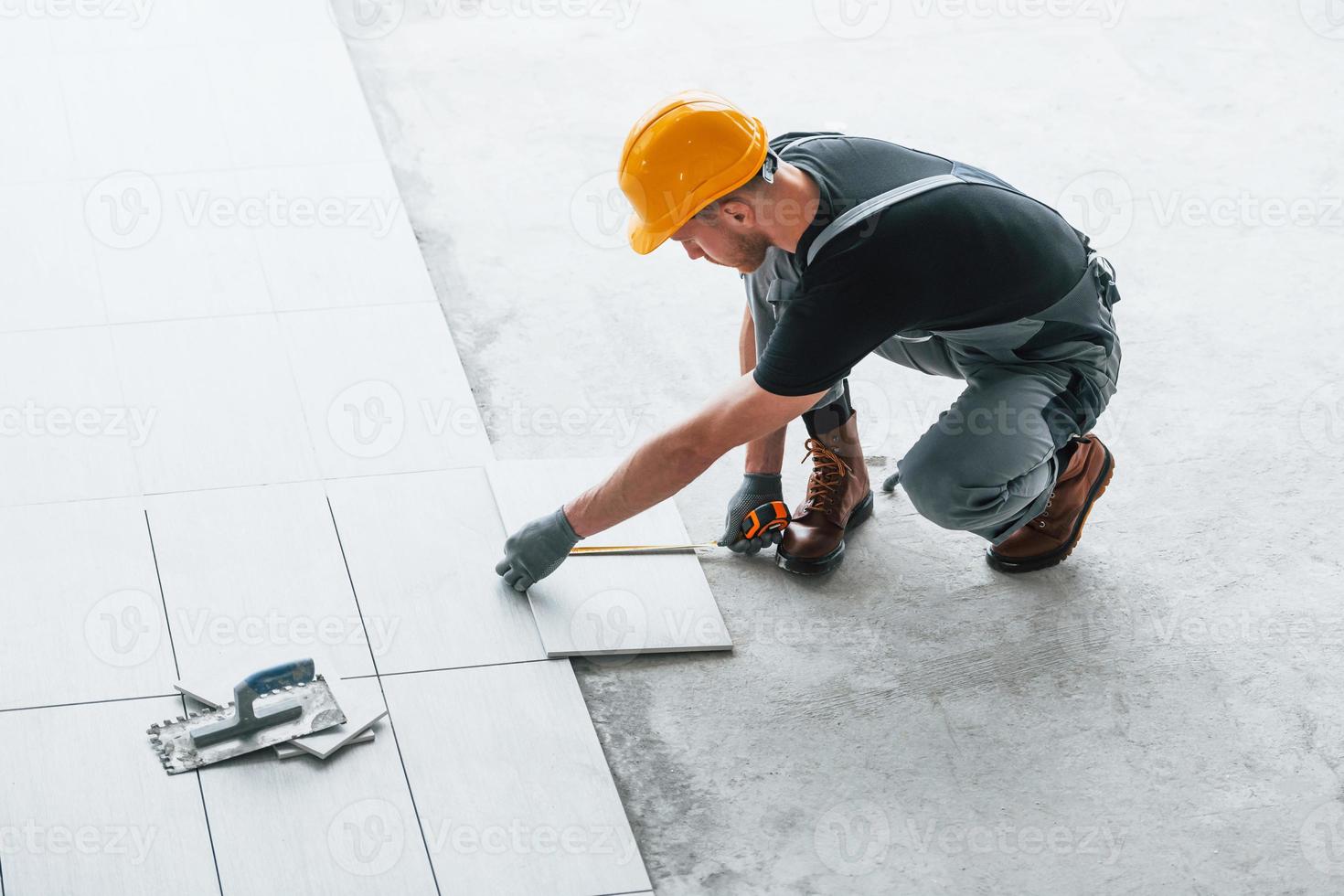 Installation of plates. Man in grey uniform and orange hard hat works indoors in modern big office at daytime photo