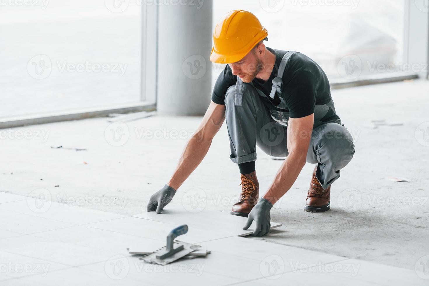 Installation of plates. Man in grey uniform and orange hard hat works indoors in modern big office at daytime photo