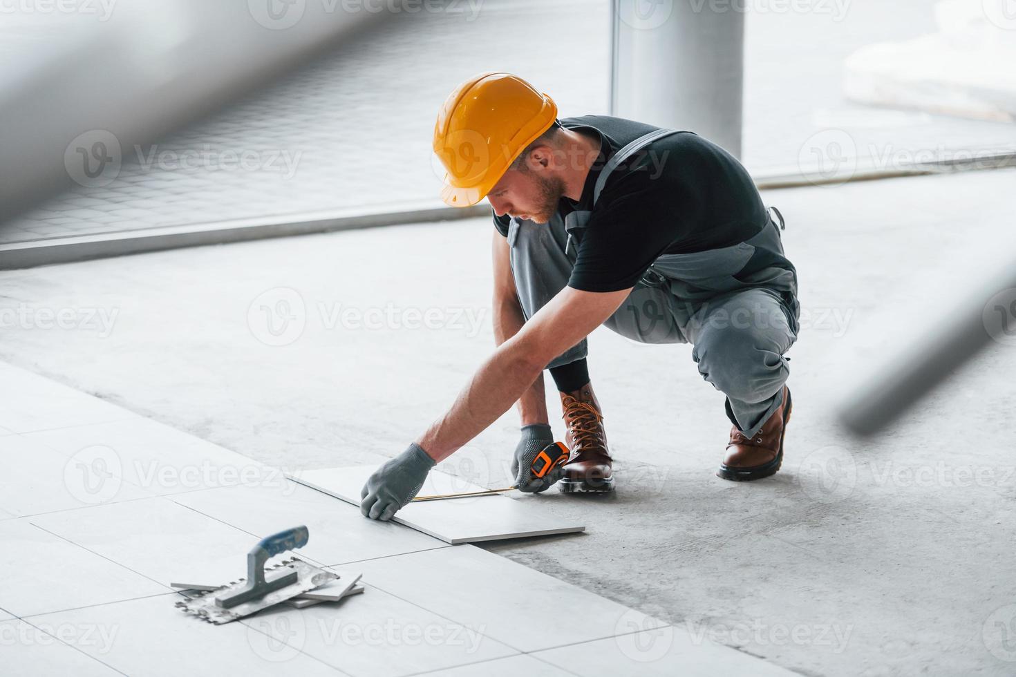 Installation of plates. Man in grey uniform and orange hard hat works indoors in modern big office at daytime photo