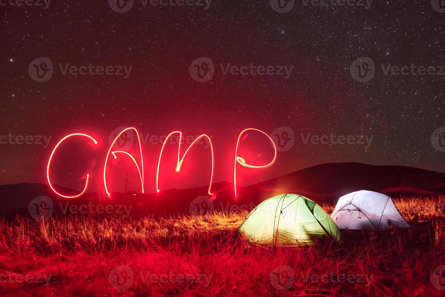 Red neon camp word. Two iluminated tents under stars at mountains at night photo