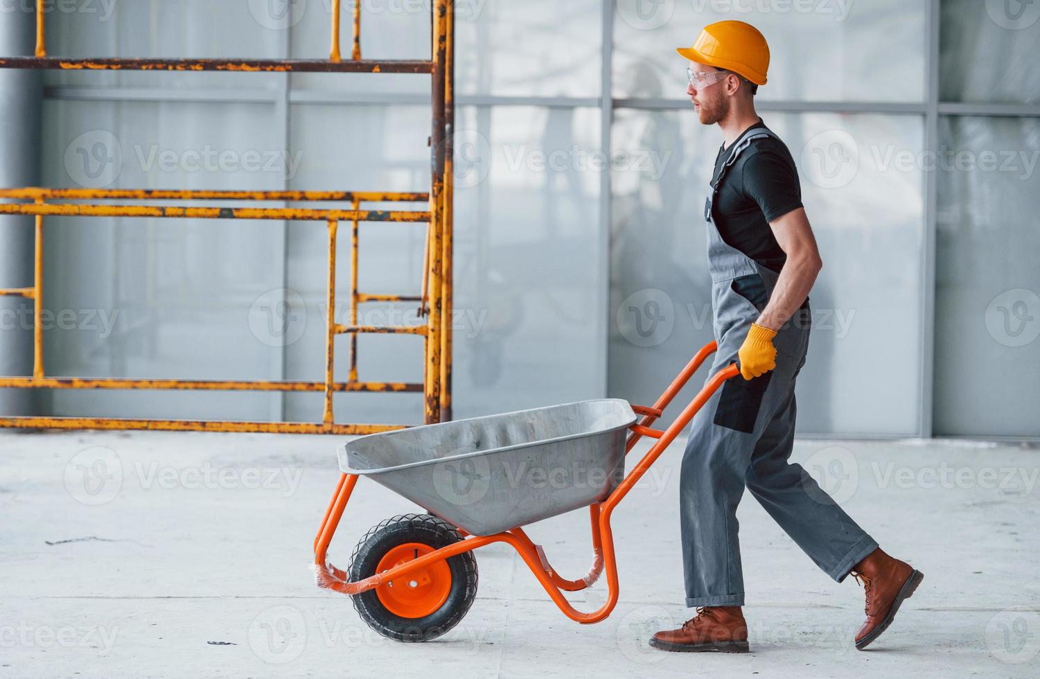 camina con carretillas. el hombre con uniforme gris trabaja en el interior de una gran oficina moderna durante el día foto