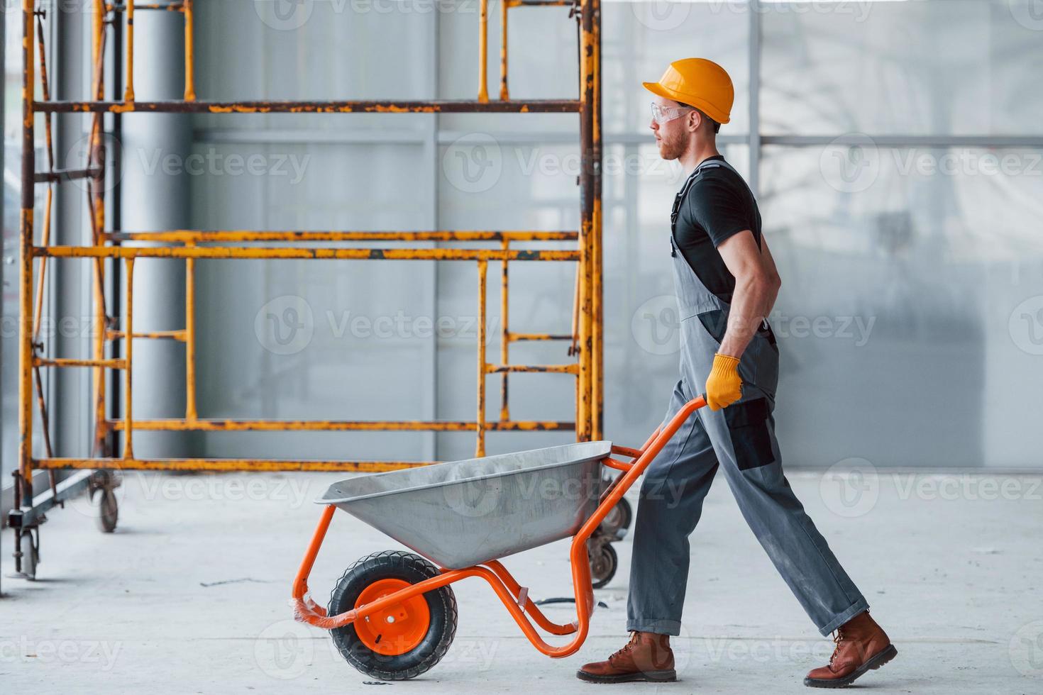 Walks with wheelbarrows. Man in grey uniform works indoors in modern big office at daytime photo