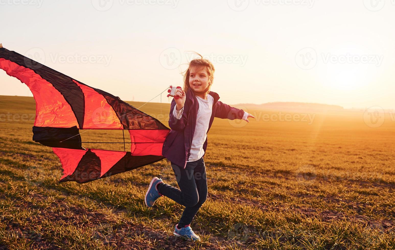 niña feliz corriendo con cometa en las manos en el hermoso campo a la hora del sol foto