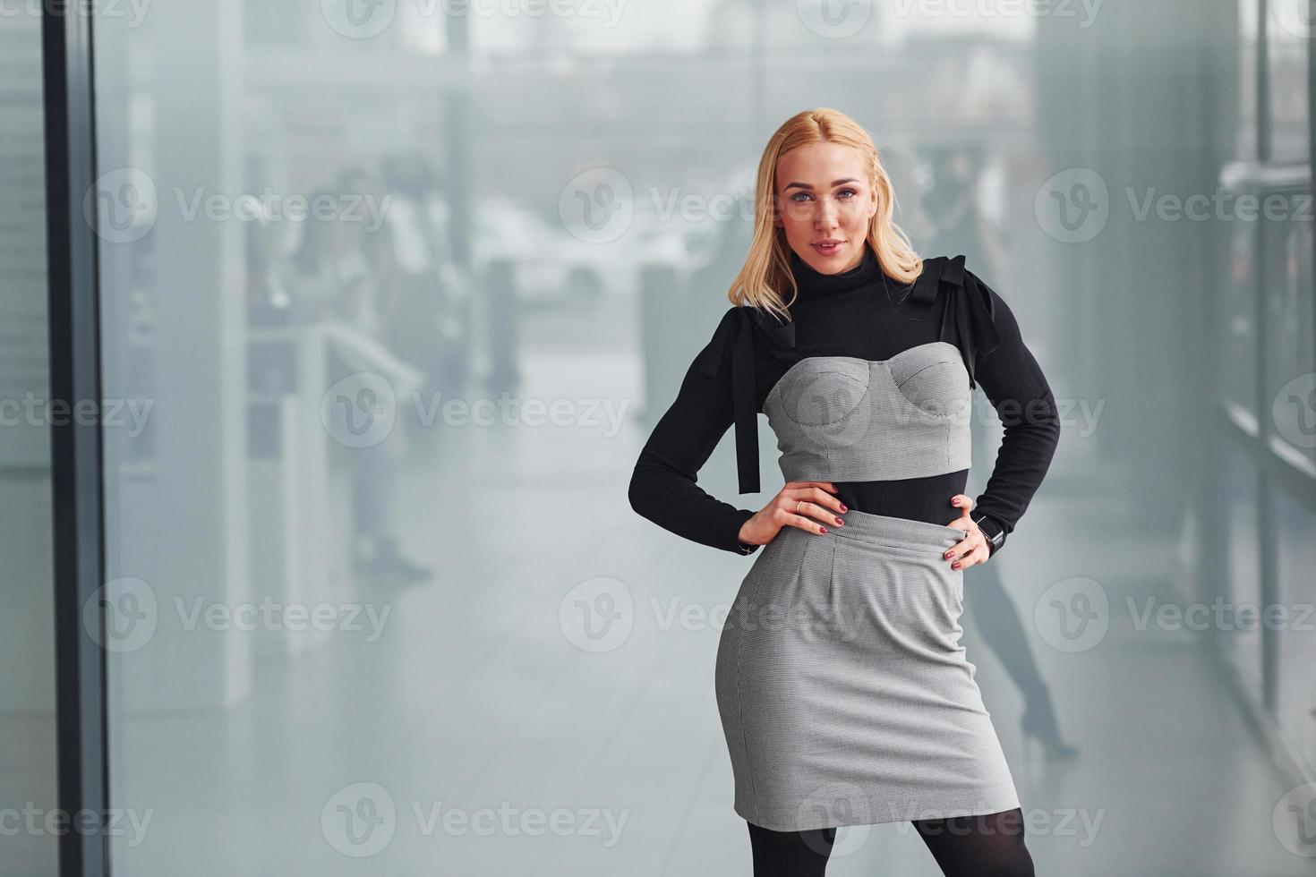 Portrait of beautiful blonde in elegant clothes that standing indoors against grey background photo