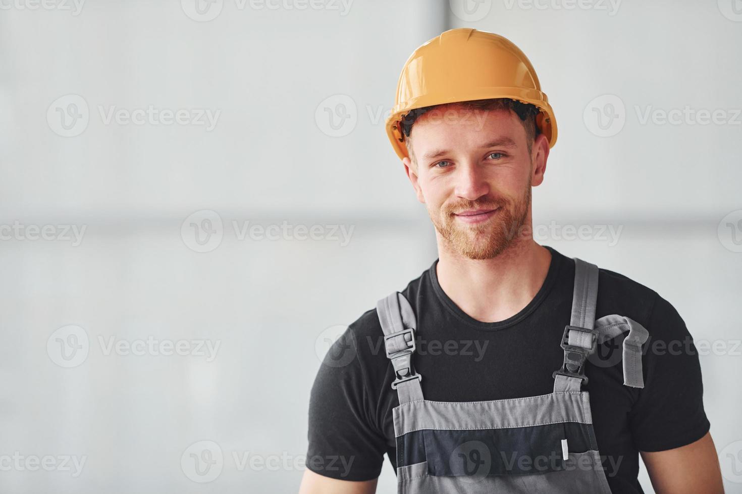 retrato de un hombre con uniforme gris y casco naranja que está parado en el interior de una gran oficina moderna durante el día foto