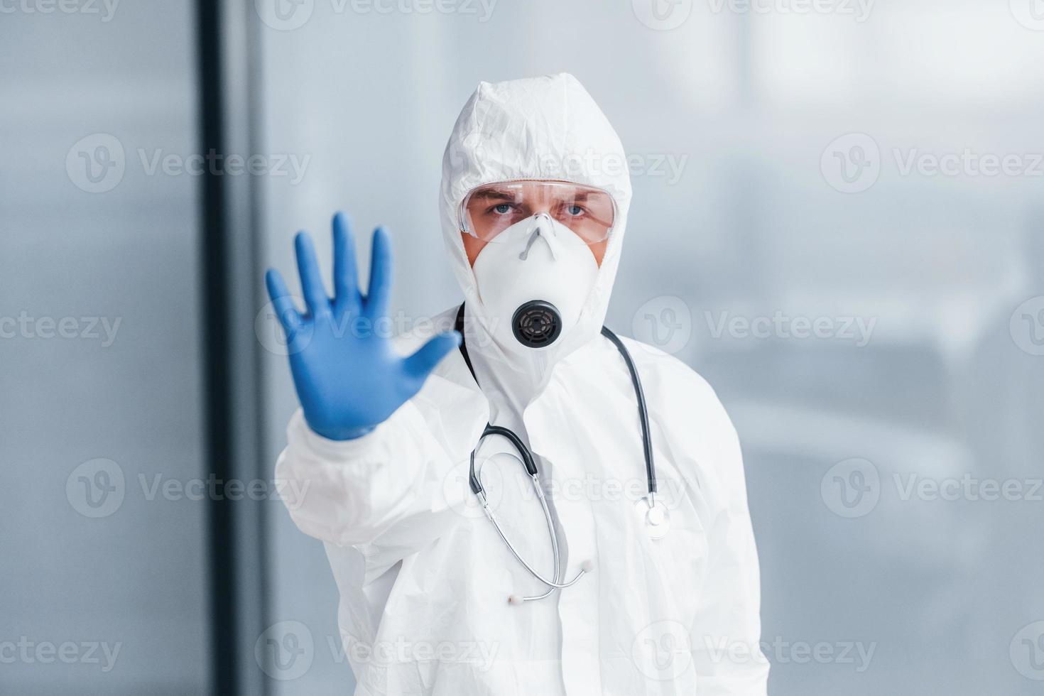 muestra el gesto de parada a mano. médico científico masculino en bata de laboratorio, anteojos defensivos y máscara foto