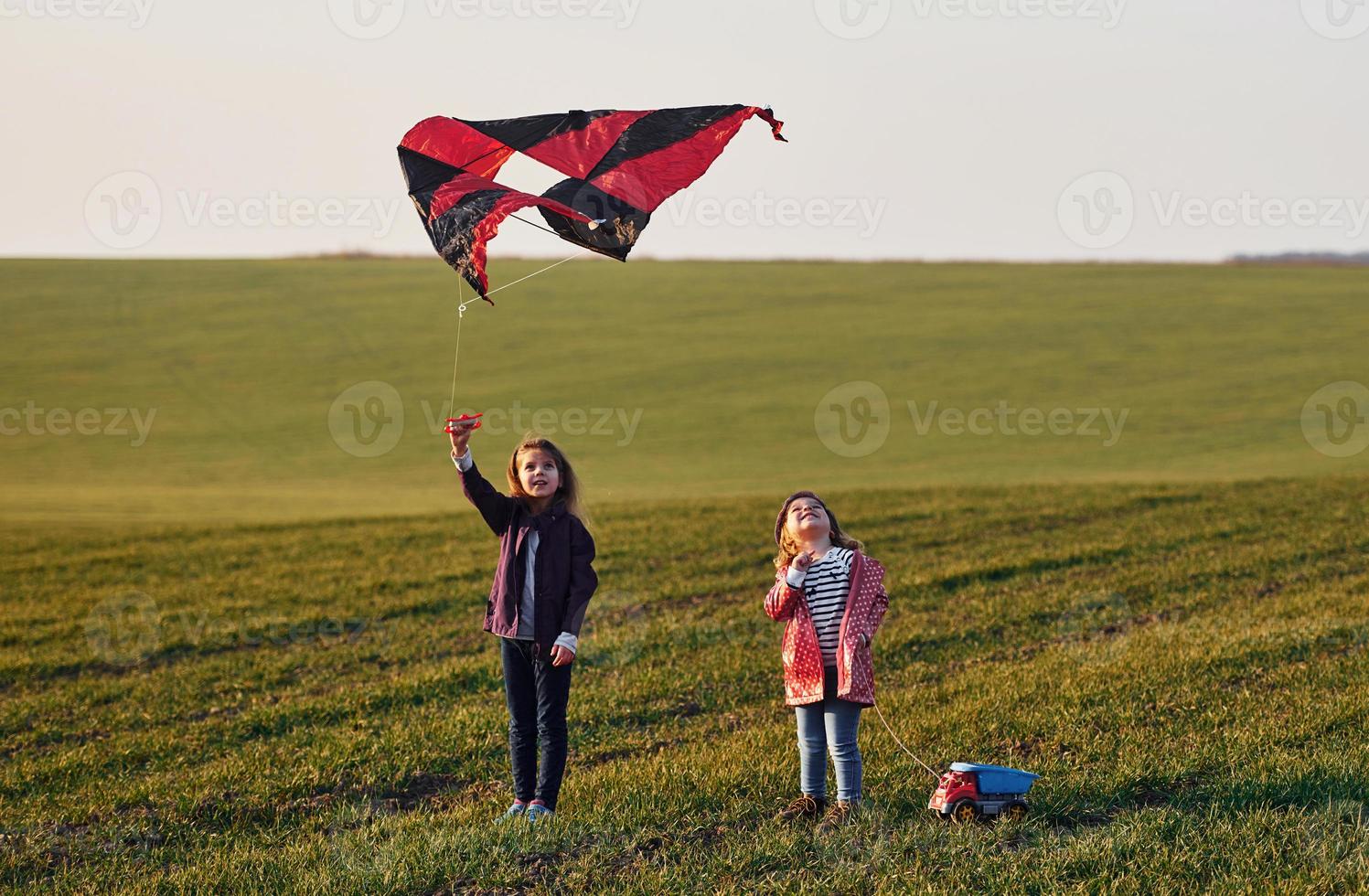 Two little girls friends have fun together with kite and toy car on the field at sunny daytime photo
